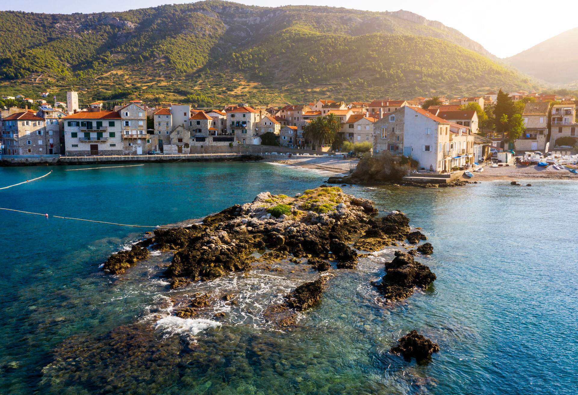 A coastal town lying at the foot of a hill surrounded by clear turquoise waters.
