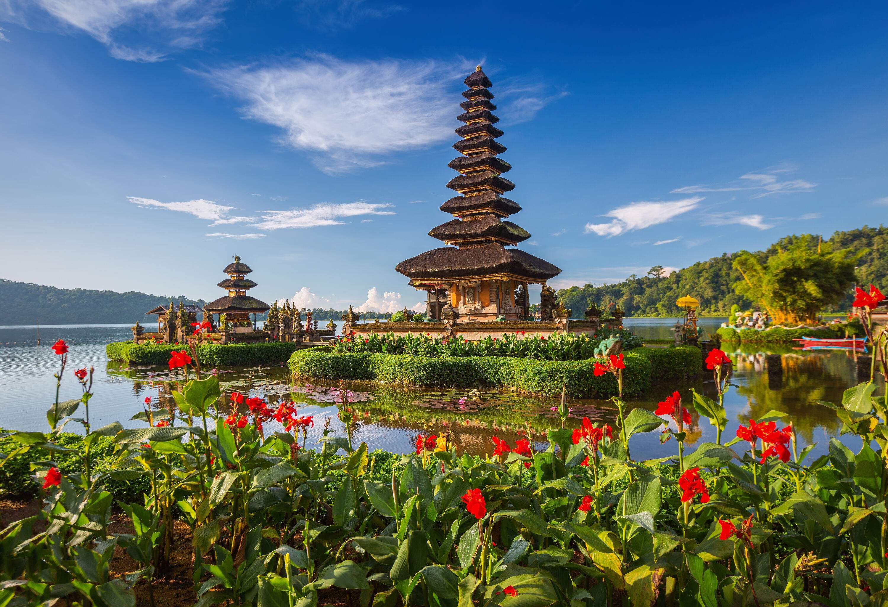 Pura Ulun Danu Bratan is a Hindu temple with multilevel pagoda-style thatched roofs nestled beside a lake and surrounded by a flower garden.
