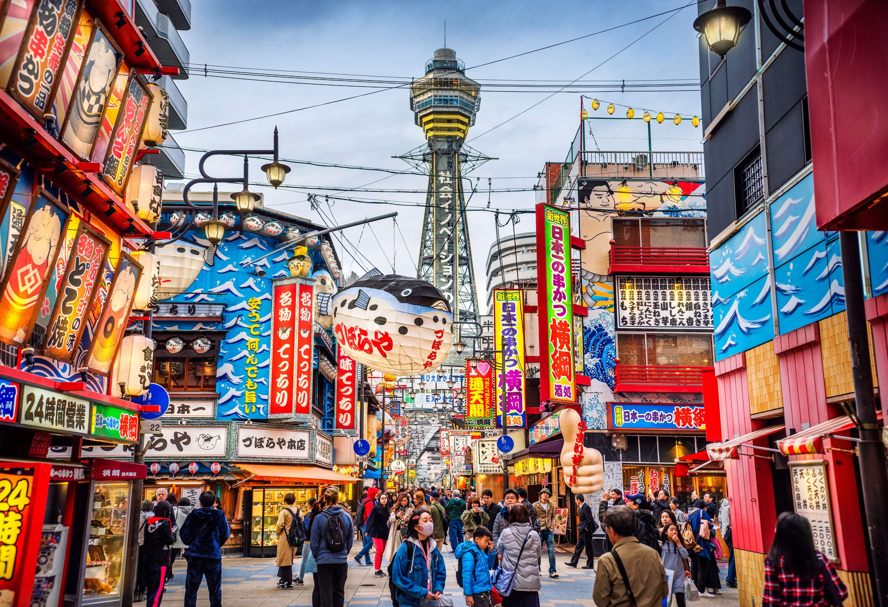 A vibrant neighbourhood decorated with unique signs and the Osaka Tower in the background.