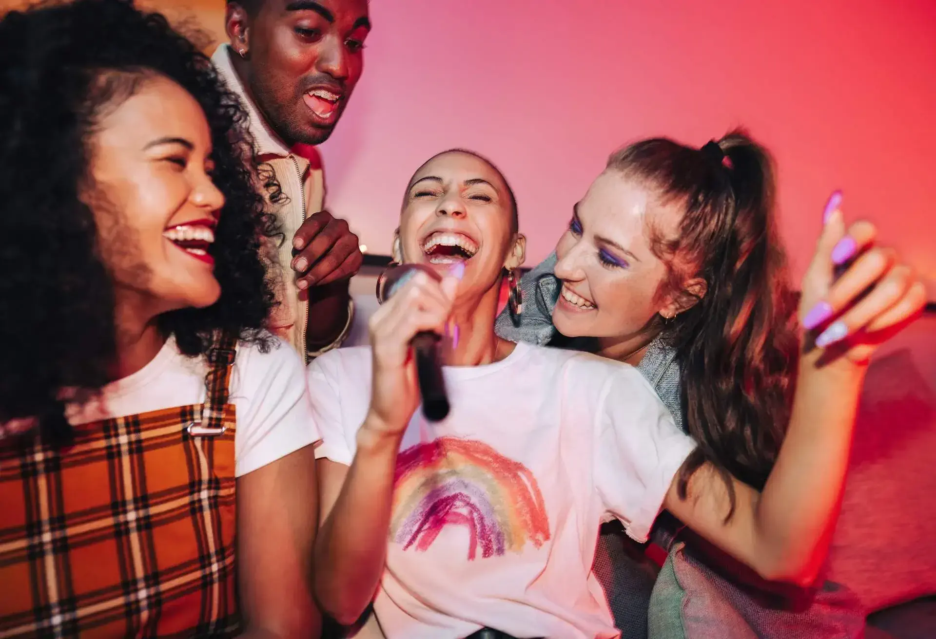 Joyful friends singing their favourite song during karaoke night. Happy young friends laughing joyfully at a house party. Group of multicultural friends having a good time on the weekend.