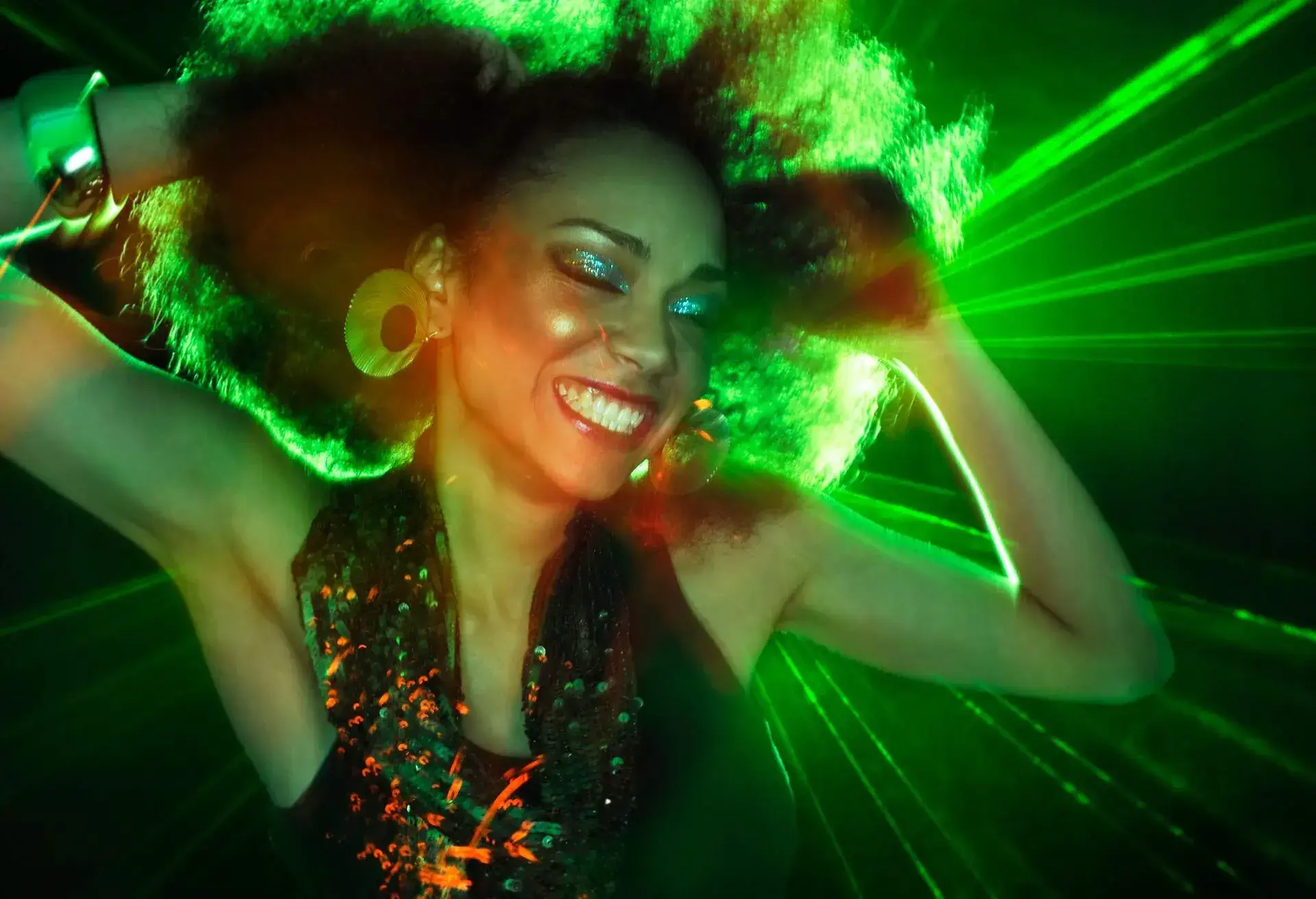A person dances with their eyes closed, lost in the rhythm and movement as they sway and groove against a backdrop of bright and vibrant lights.