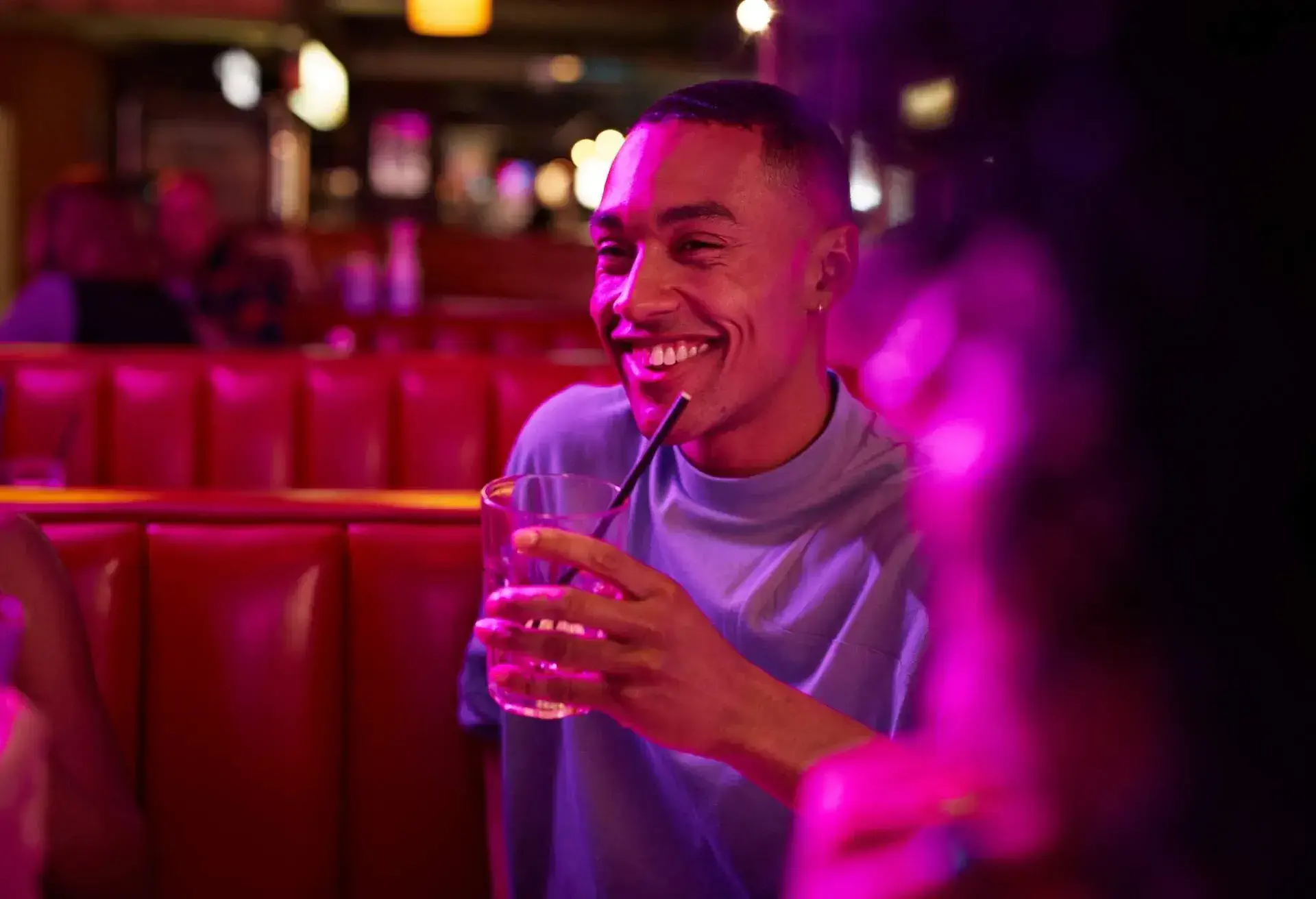 A man seated in a booth, holding a drink and smiling.