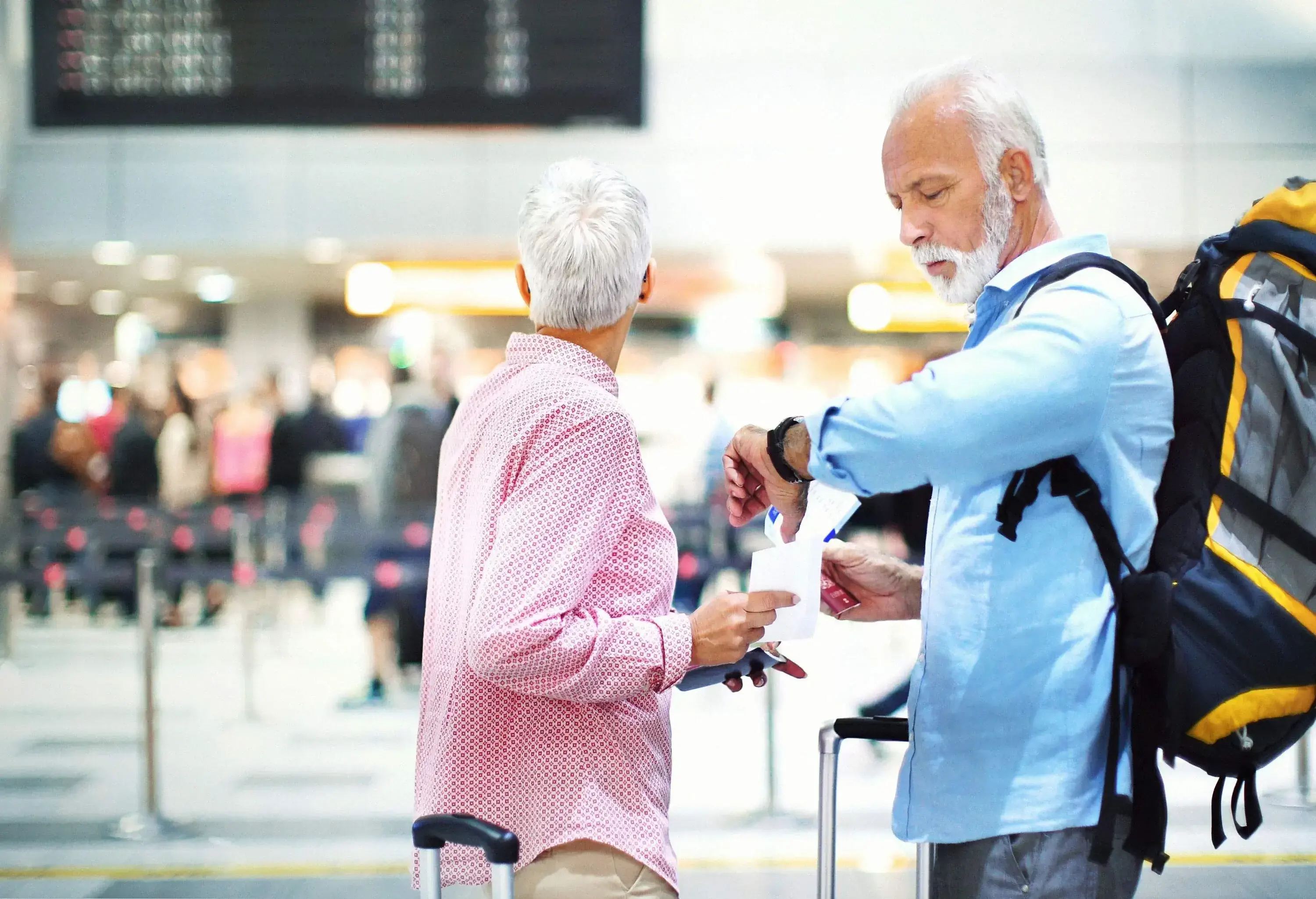 A senior couple arriving at the airport and waiting by the departures board.