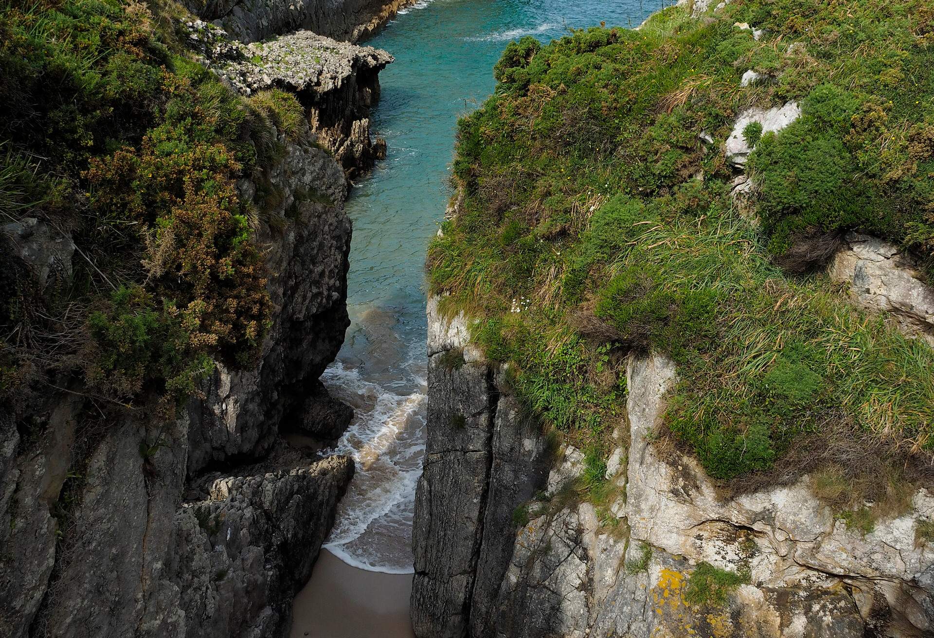 Eroded rocky coastline and small beach at Playa de Gulpiyuri near the small town of Nueva de Llanes, Principado de Asturias, North of Spain on the shore of the Cantabrian Sea and the Bay of Biscay.