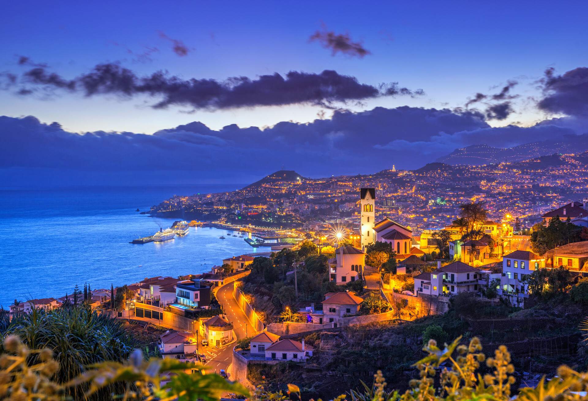 Mountains fully packed with lit houses and buildings along the scenic bay over dramatic clouds.