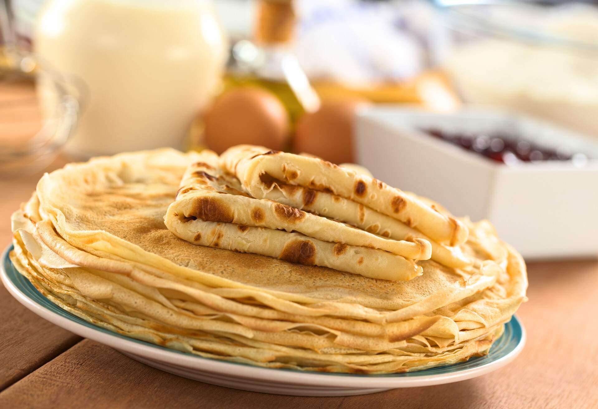 Fresh homemade crepes on plate with ingredients and strawberry jam in the back (Selective Focus, Focus on the front edge of the lower folded crepe); Shutterstock ID 103657649; Purpose: ; Brand (KAYAK, Momondo, Any):