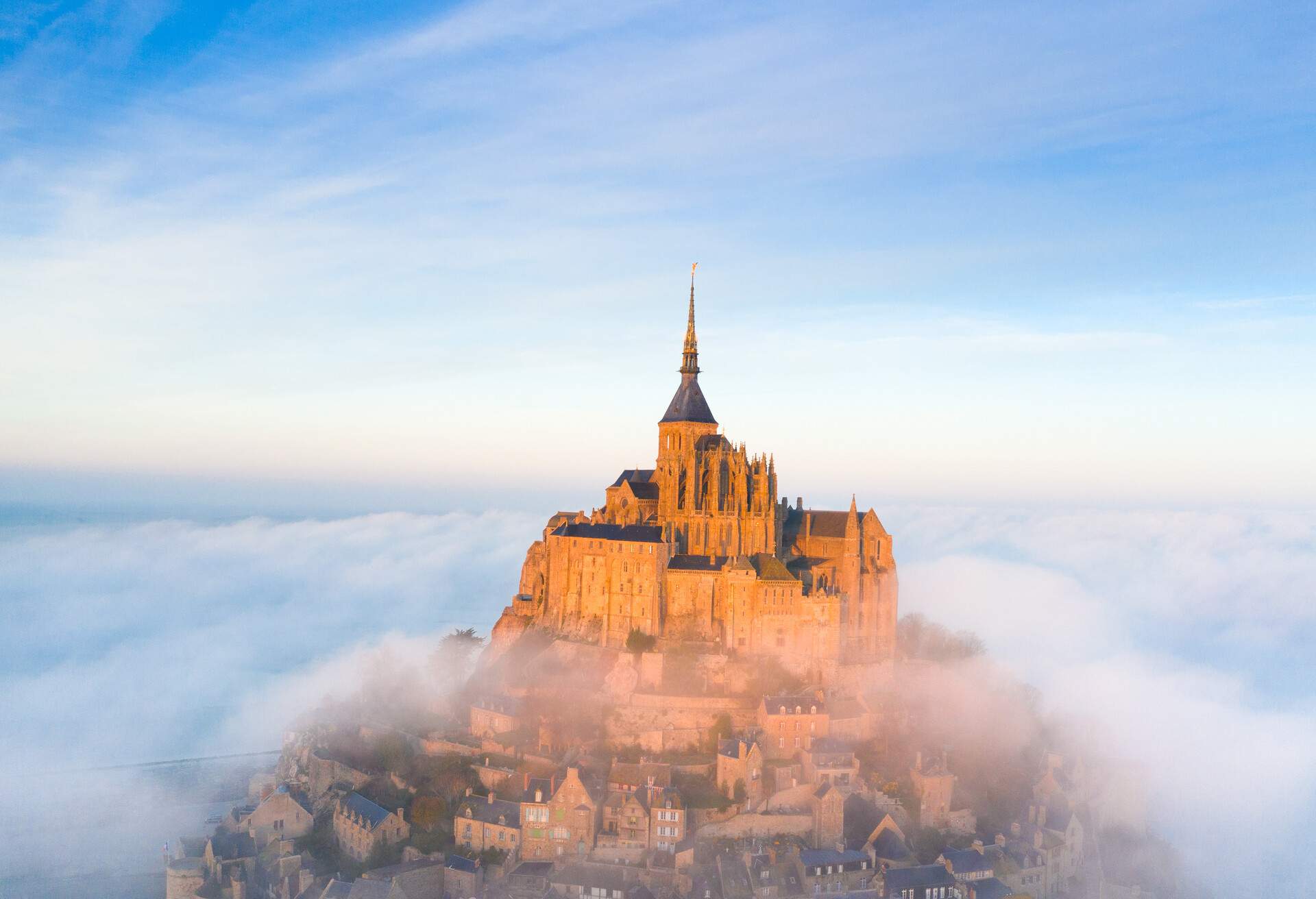 This image is taken in the Mont Saint-Michel during the high tides with fog. It's the sunrise  You can see the Couesnon on the foreground. The Mont Saint-Michel is in the light..It's an aerial photo.