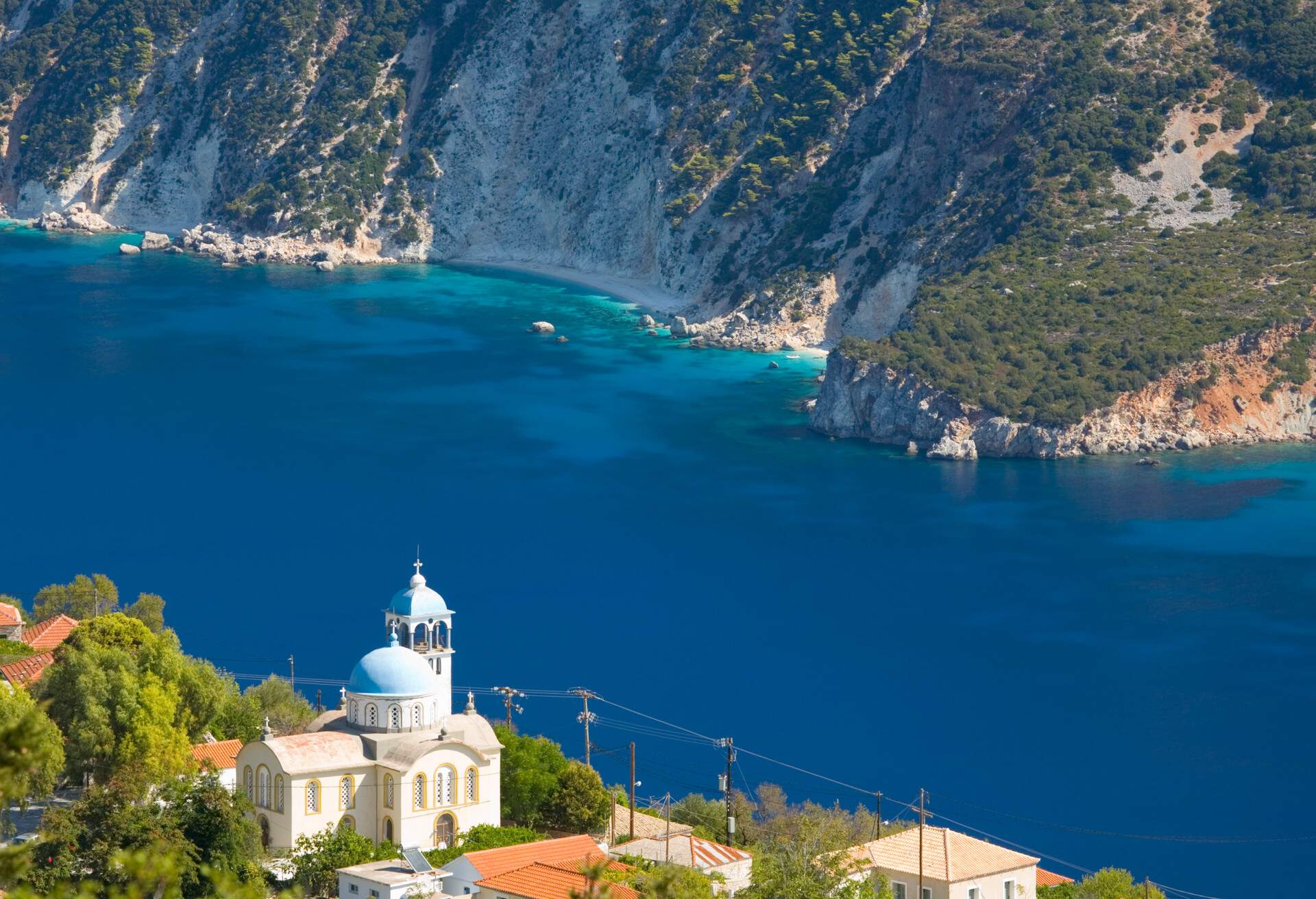 Village houses and church precariously perched above the deep blue waters of Afales Bay, Exogi, Ithaca (aka Ithaki, Ithaka), Ionian Islands, Greece, Europe.