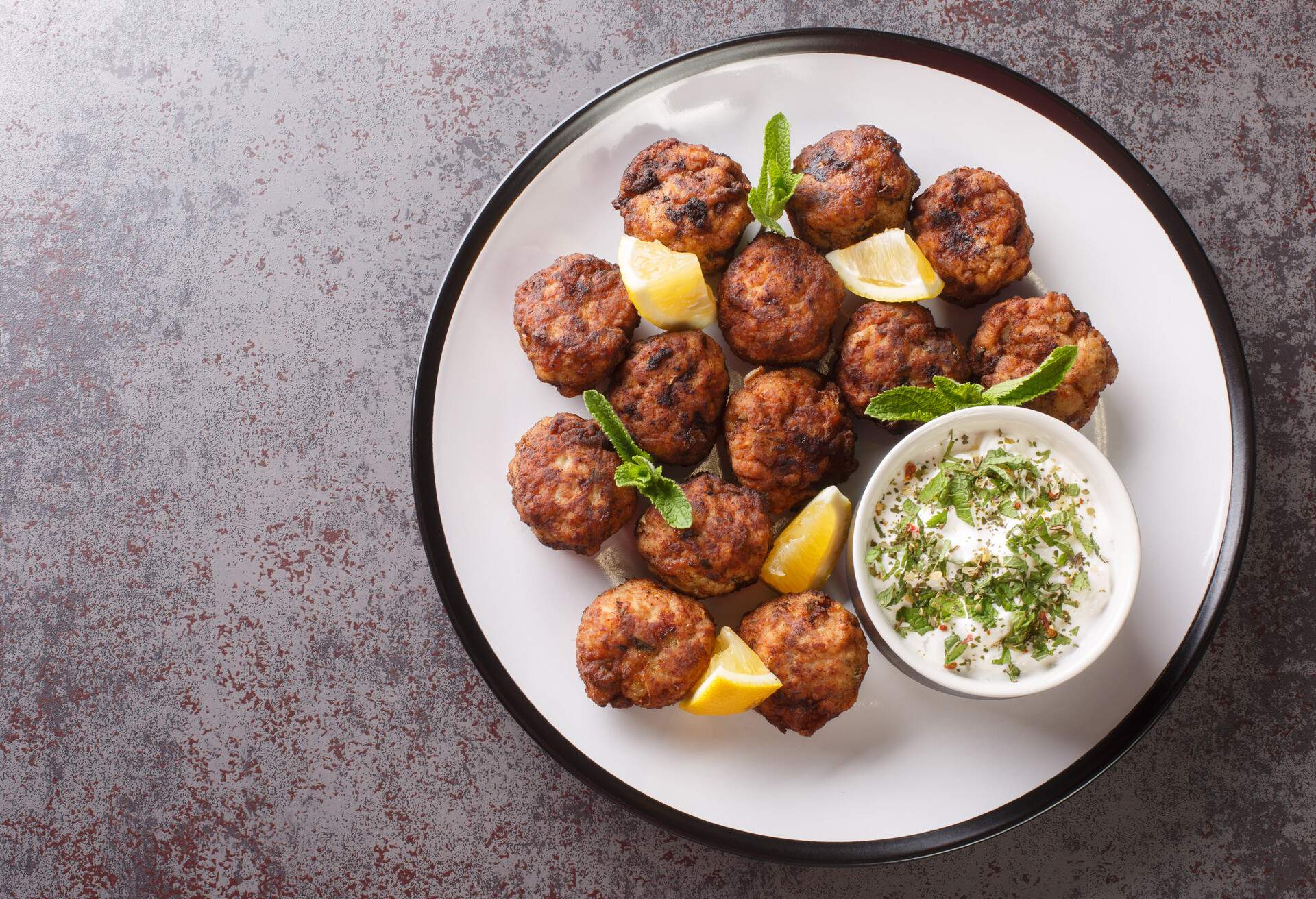 Keftedakia is a Greek traditional dish that is created with minced beef and bread crumbs rolled into balls and fried closeup on a white plate on a table. Horizontal top view from above