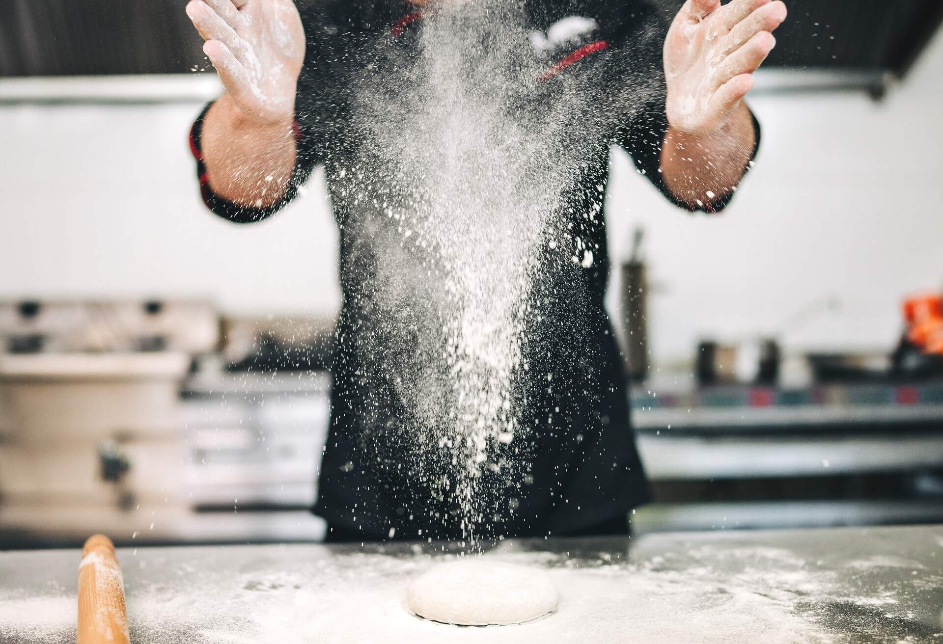 Chef baker preparing a pizza in the italian restaurant. He use fresh products, and throwing flour in the air