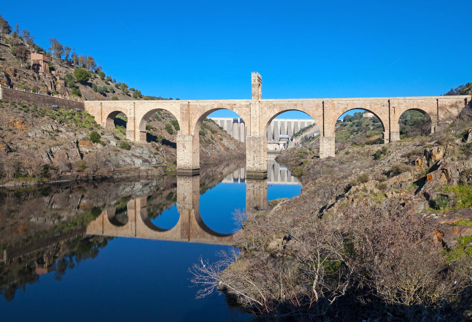 Alcántara Bridge over the Tagus River at Alcántara (Extremadura, Spain). Its a Roman stone arch bridge, built between 104 and 106 AD. In the background is seen the dam of the Alcántara reservoir.