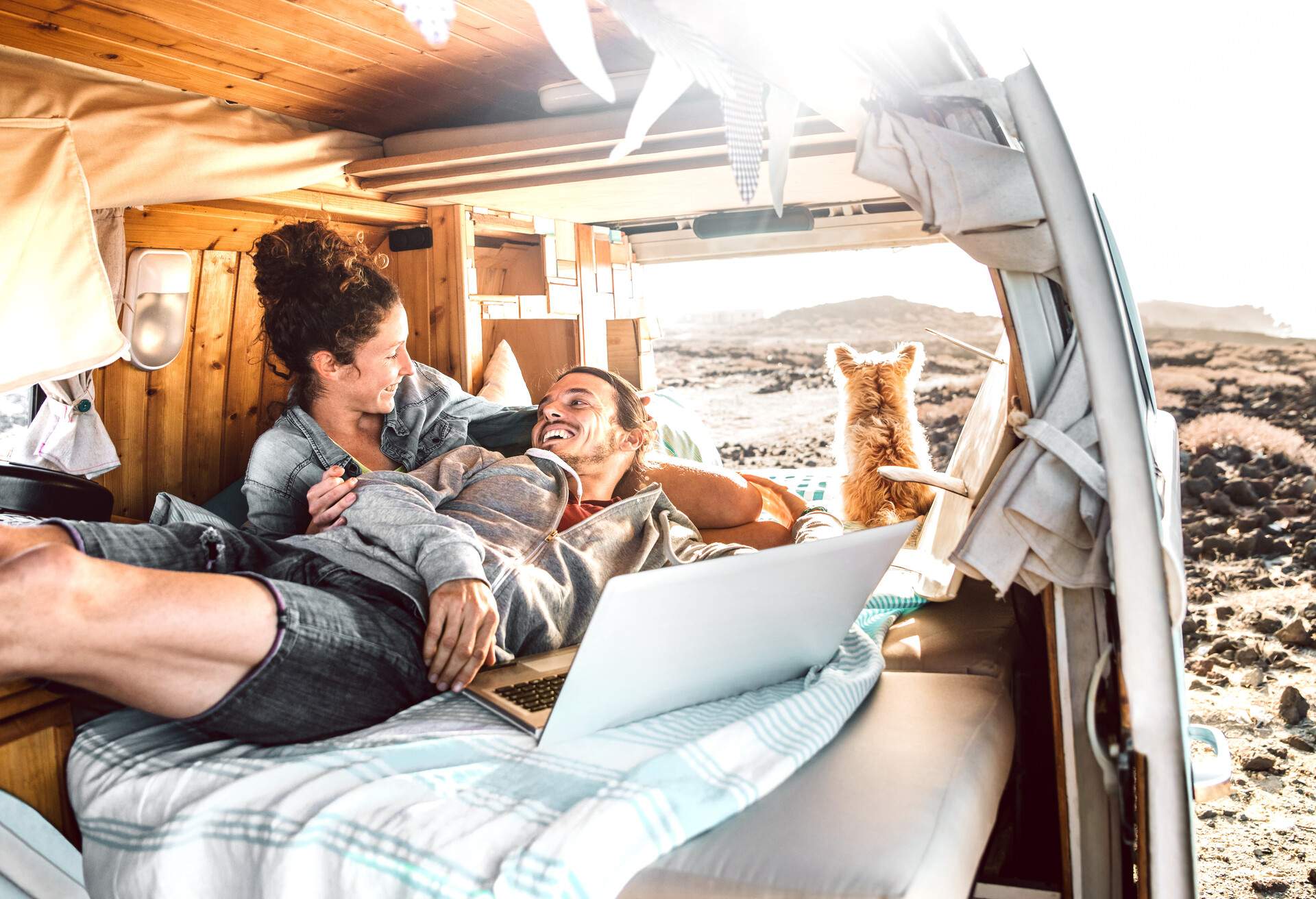 Hipster couple with dog traveling together on retro mini van transport - Digital nomad concept with indie people on minivan romantic trip working at laptop pc in relax moment - Warm contrast filter