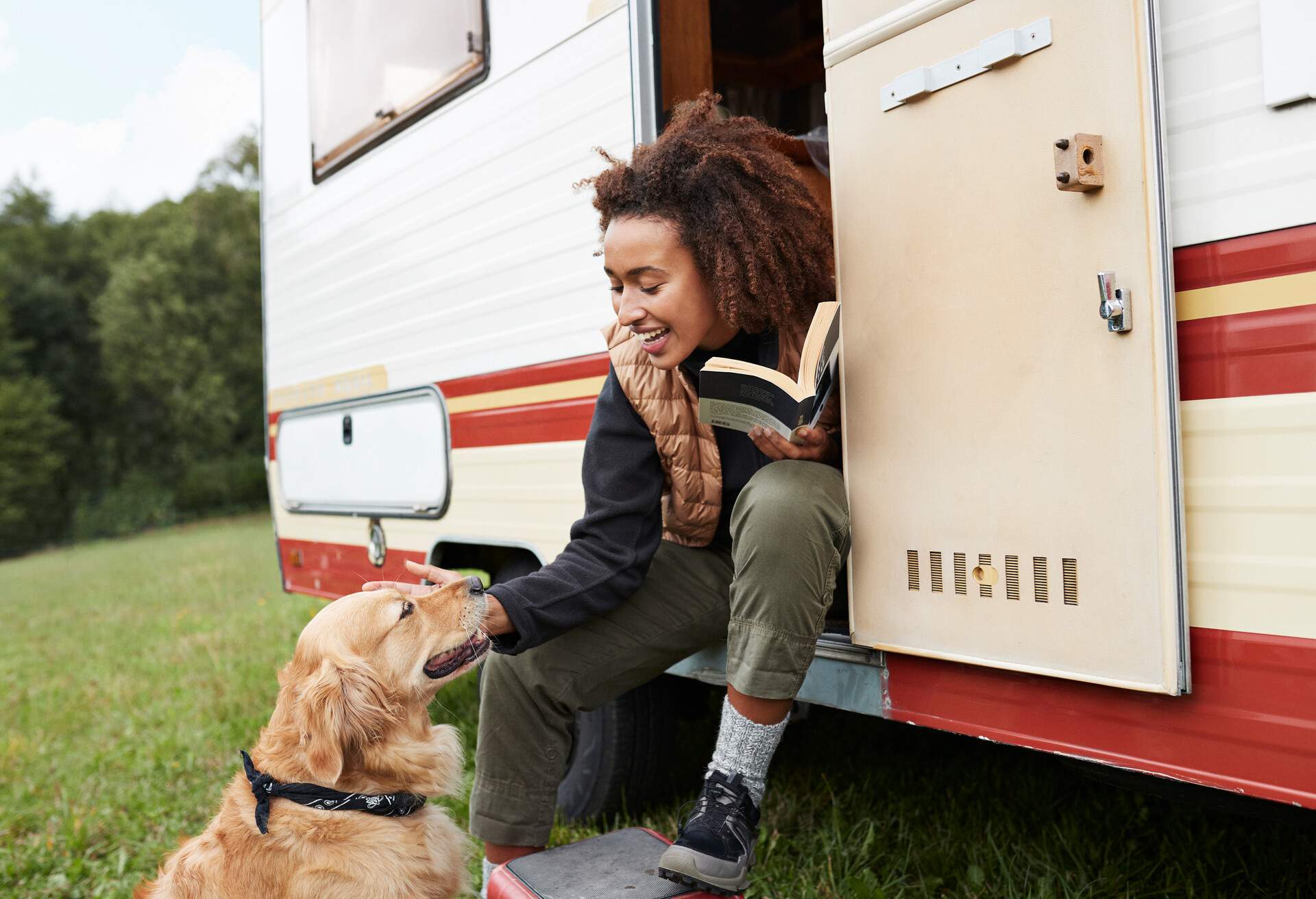 Smiling young woman stroking dog while sitting on doorway of camper van