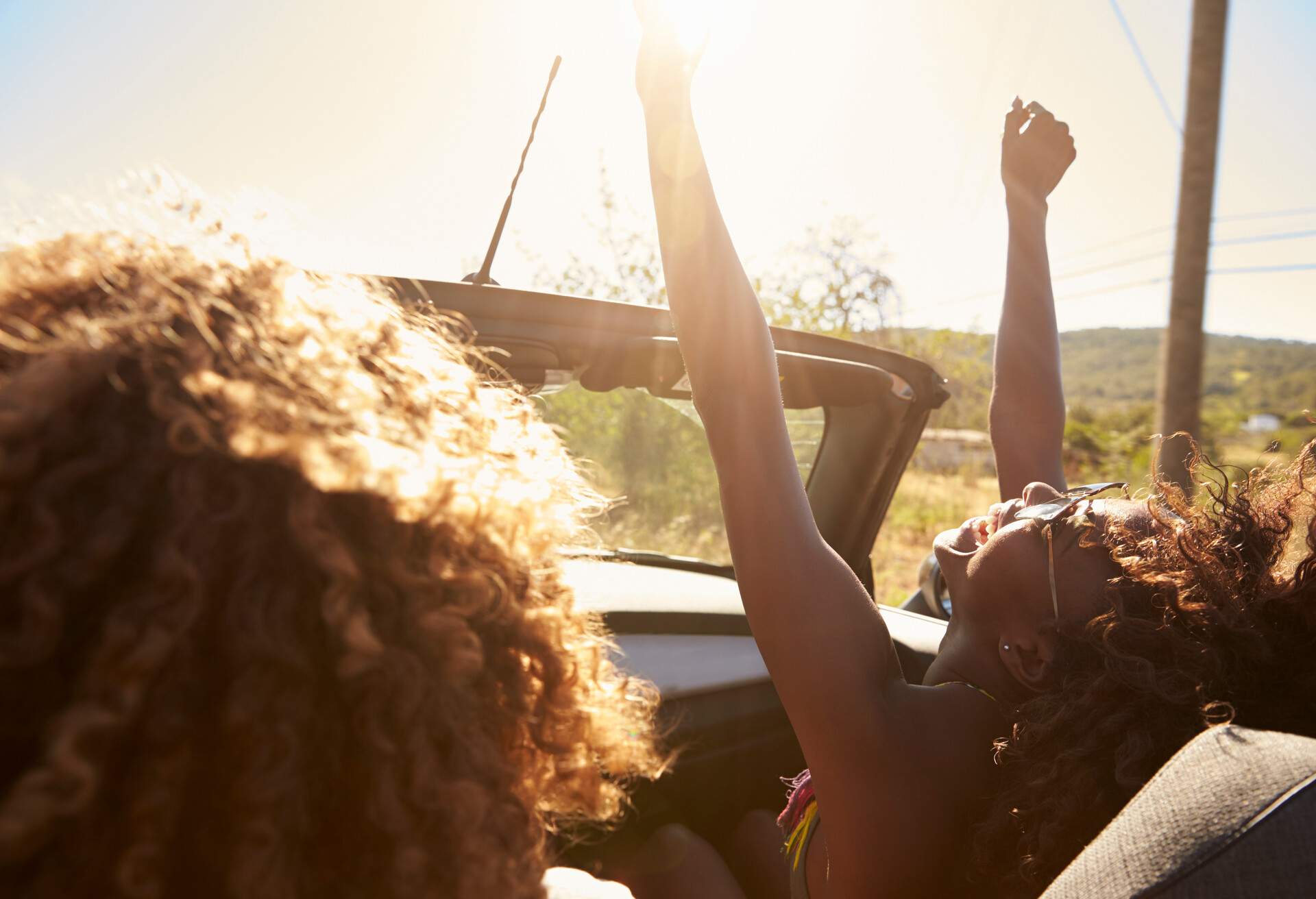 Young couple in an open top car, woman with arms raised