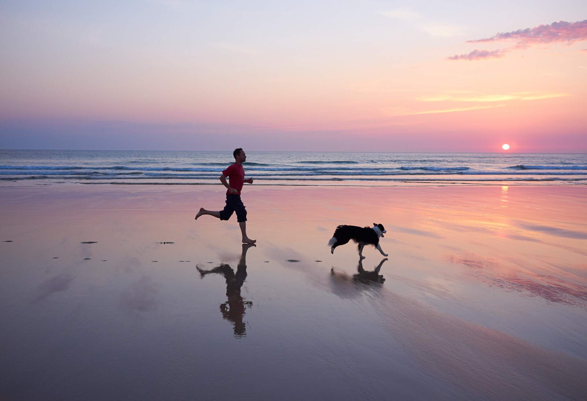 As the sun sets a figure runs along side his dog.