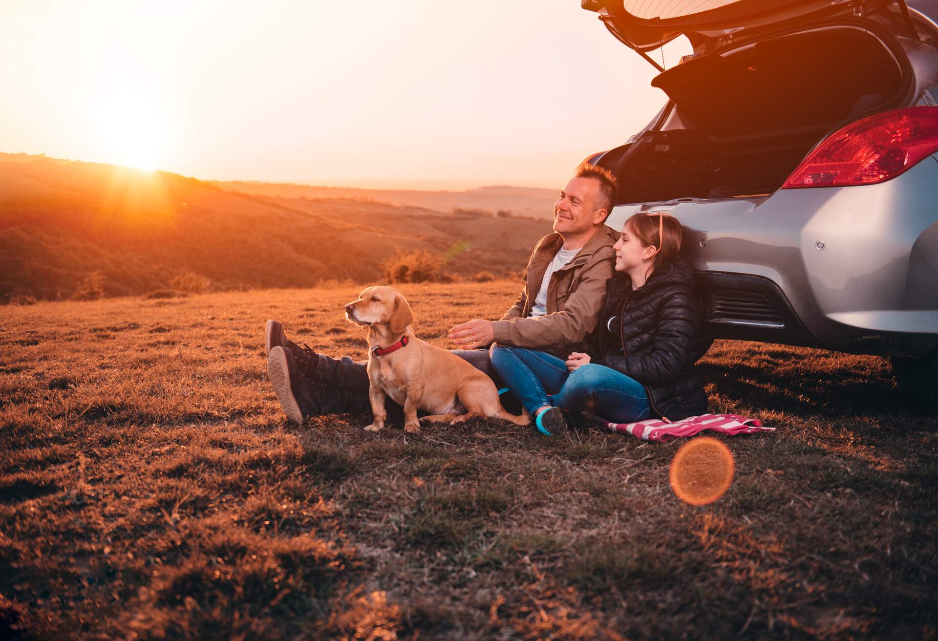 Father and daughter with small yellow dog camping on a hill while sitting on the ground by the car and having relaxing conversation; Shutterstock ID 1410313514