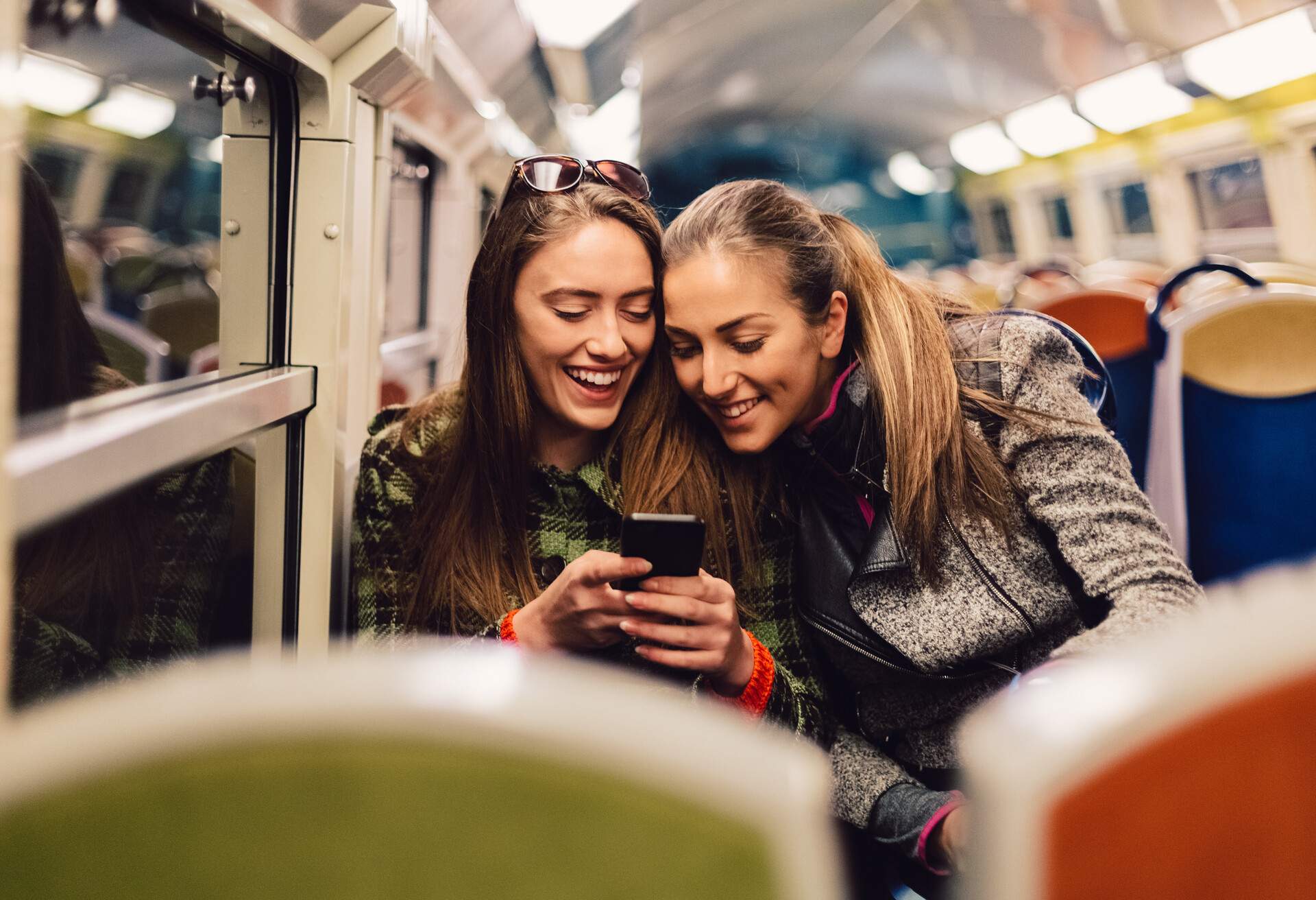 Happy friends traveling at night in public transportation and surfing the net on mobile phone