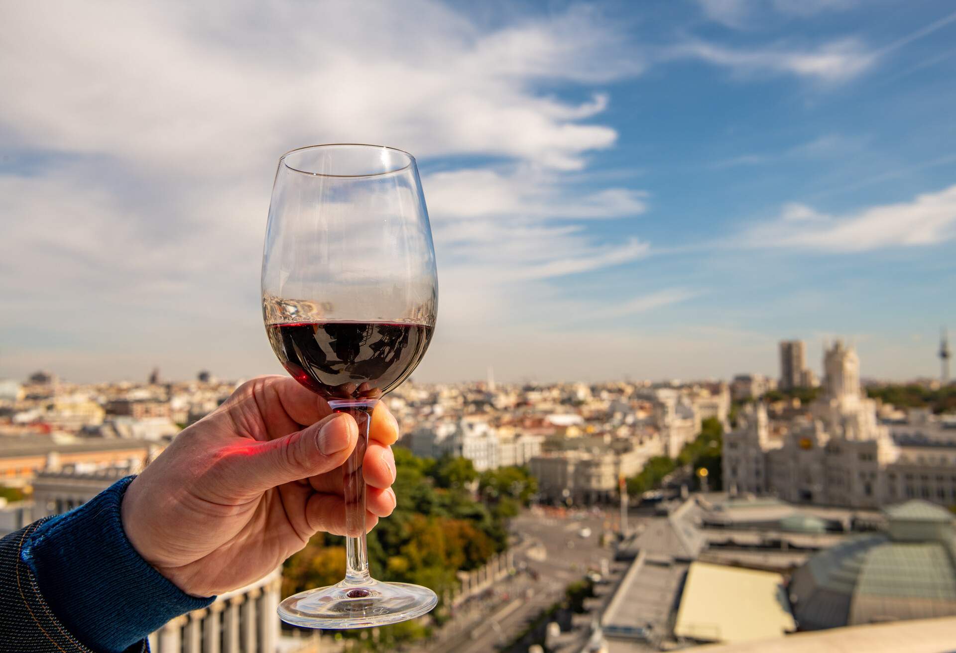 A glass of red wine held up for a toast on a rooftop overlooking the beautiful cityscape of Madrid, Spain.