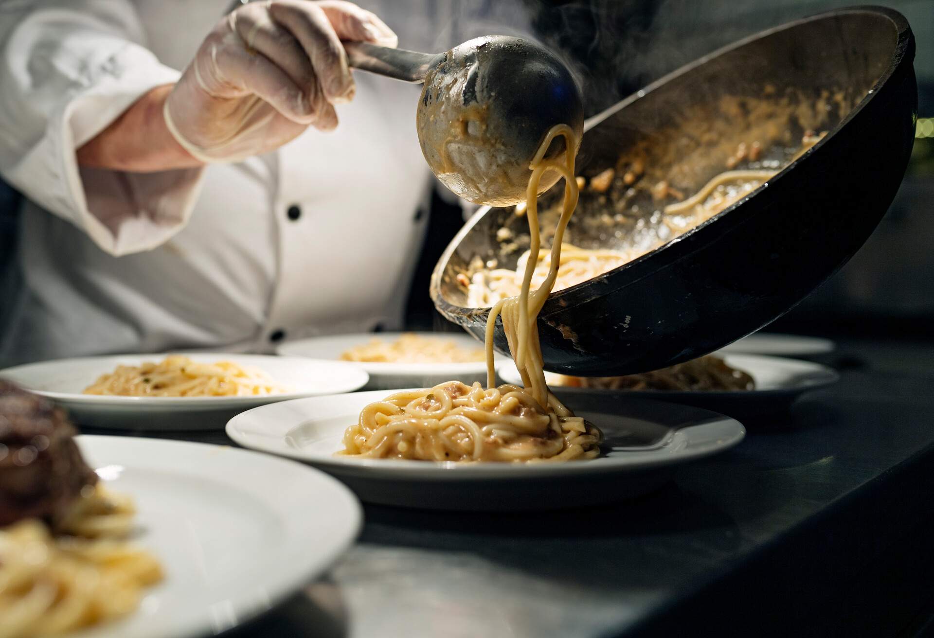 Chef pouring a serving of spaghetti with a tomato sauce from a saucepan to a plate at the pass. Photographed on location in a restaurant on the island of Møn in Denmark. Colour, horizontal with some copy space.