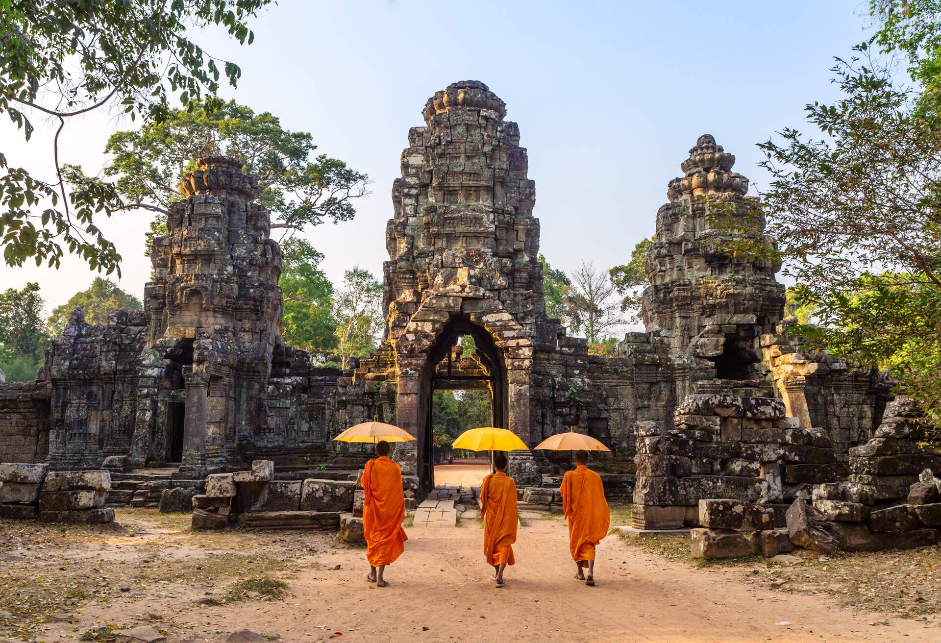 Three buddhist monks with umbrellas, walking inside Angkor Wat temple. Siem Reap, Cambodia