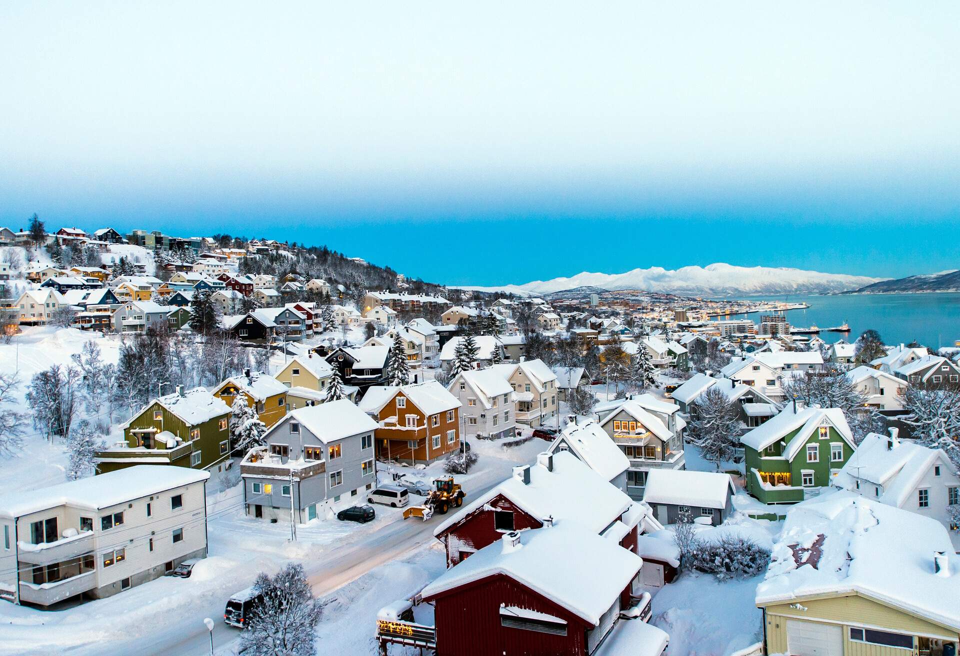 A coastal city with colourful houses and buildings covered in snow beneath a milky blue winter sky.