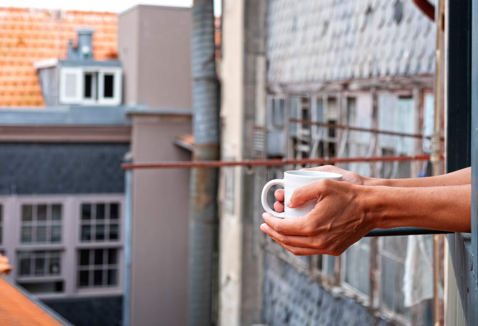 closeup of a young caucasian man having a coffee in the balcony of his home, hotel or vacation rental in the old town of a European city