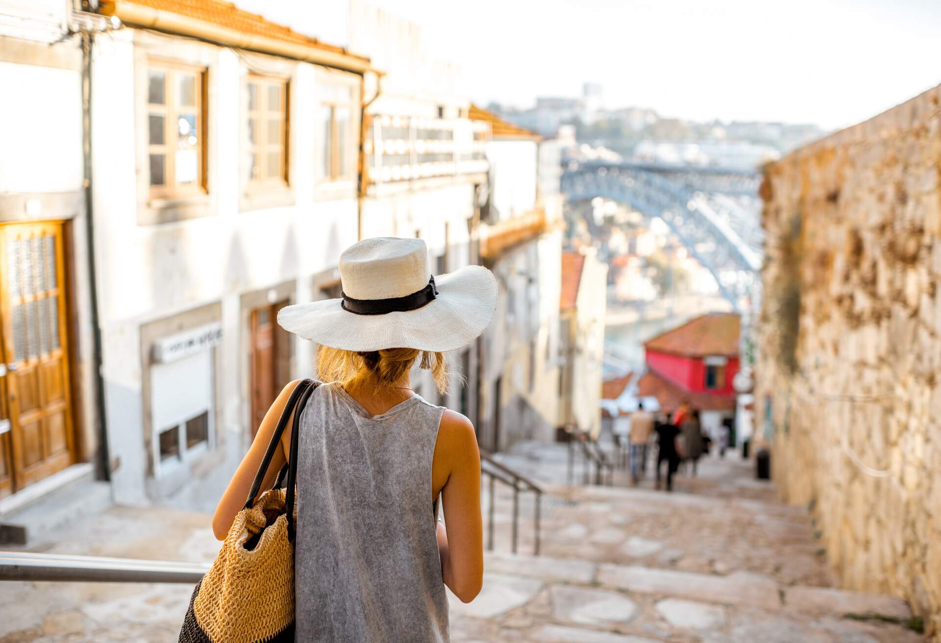 Young woman tourist walking down the stairs with famous iron bridge on the background in Porto city, Portugal