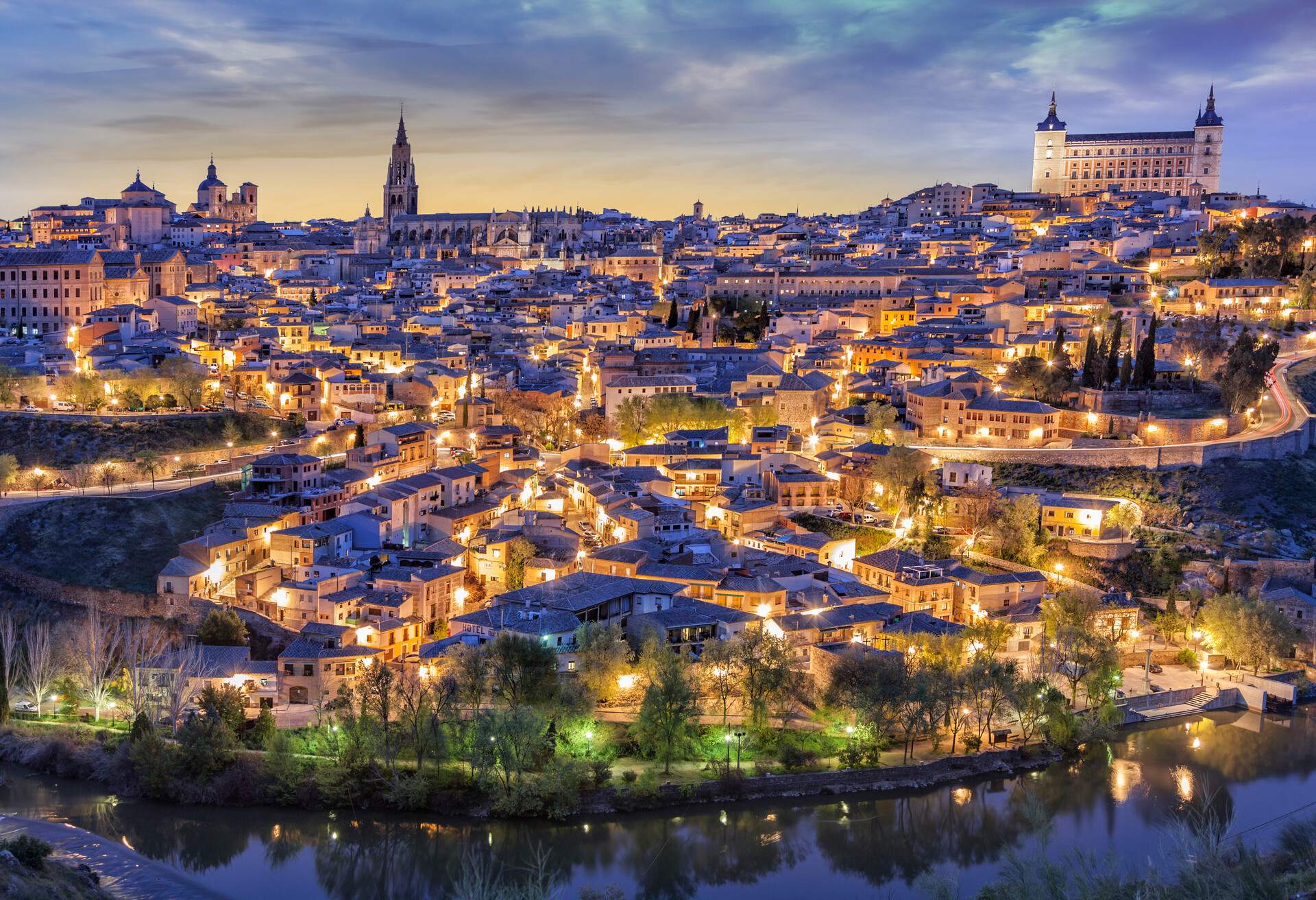 Toledo with Alcazar from the heights at dusk, with lighting and reddish sky and river.