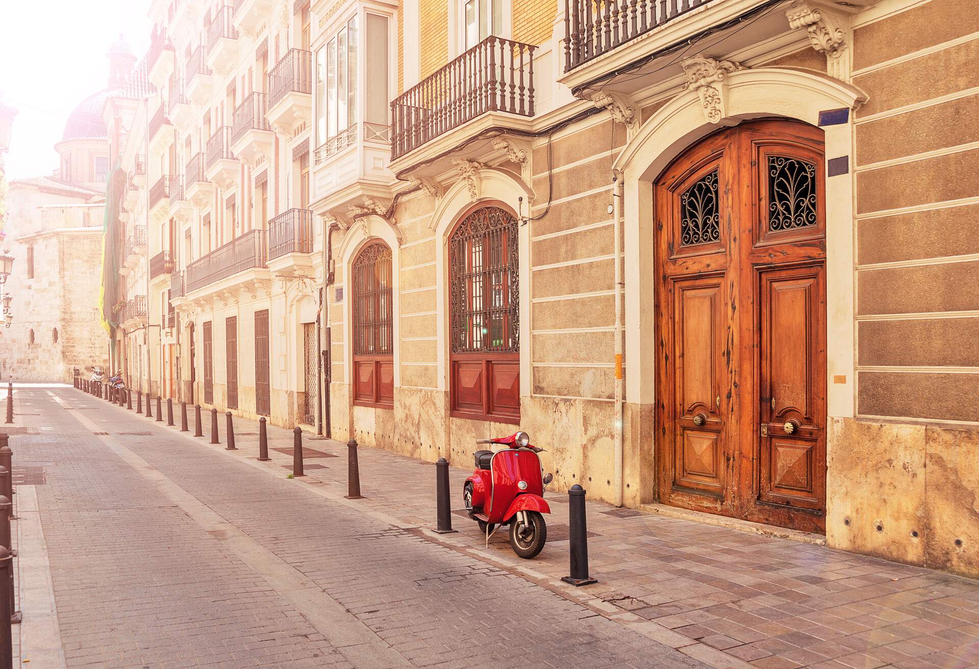 Spain. Valencia. A street in the tourist city of Valencia. Red motorcycle, moped. Tourist concept. Journey. Red vintage scooter parked on a sidewalk.