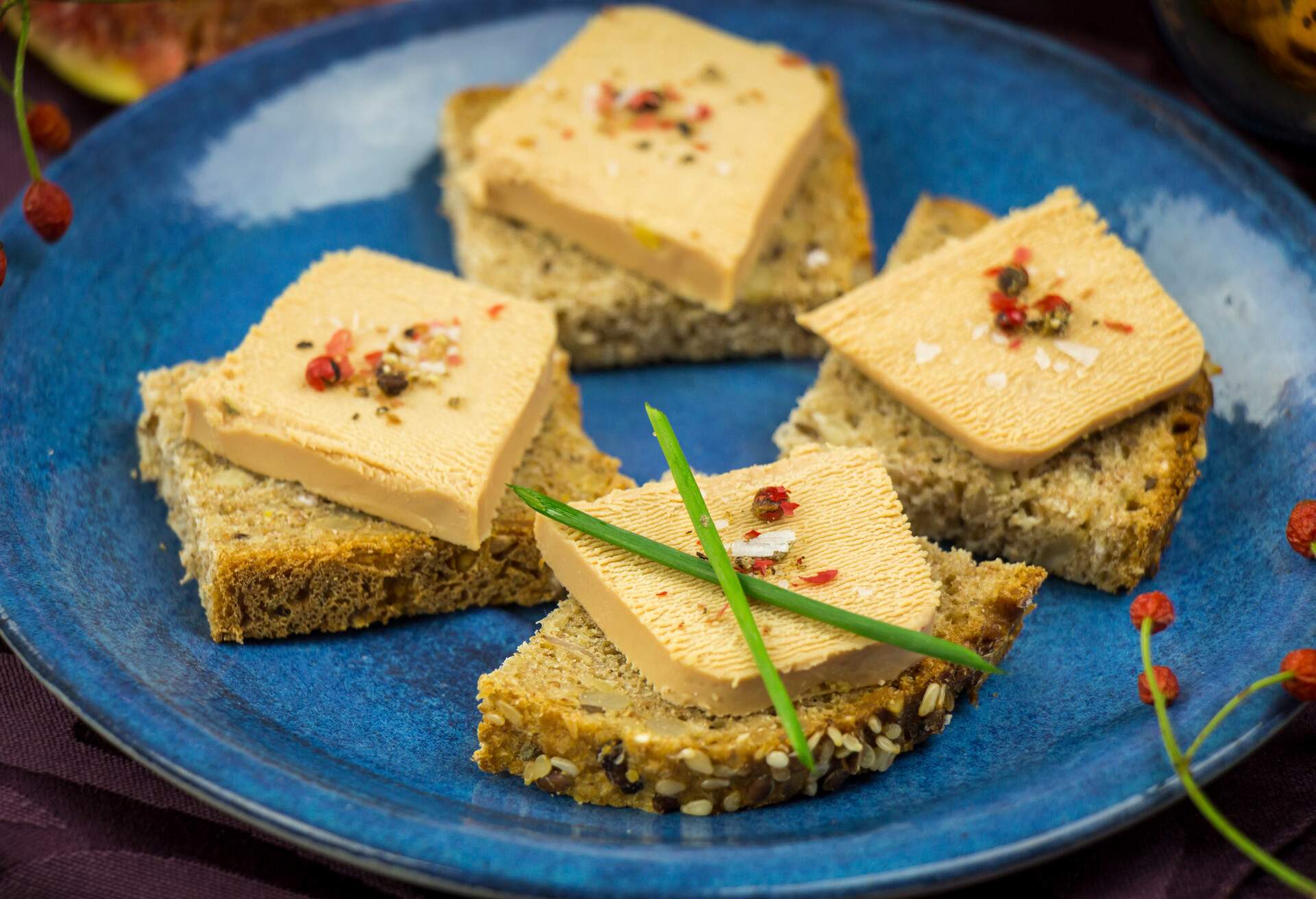 Christmas gourmet snacks with foie gras served on squares of wholegrain bread on a plate resting on a rustic burlap cloth with Xmas baubles alongside, high angle view