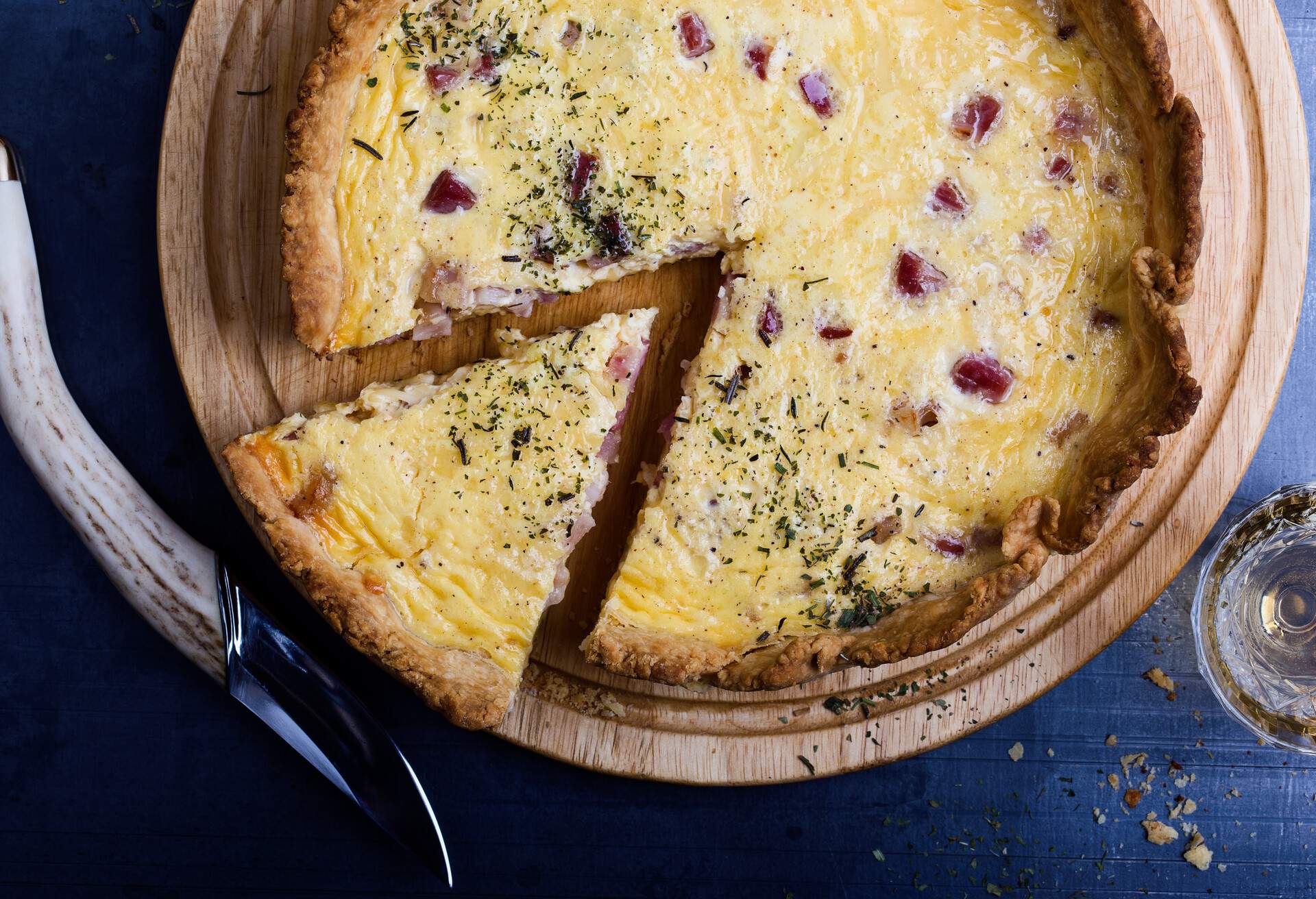 Freshly baked bacon cheddar quiche lorraine, rural savory pie sliced and ready to eat on wooden cutting board viewed from above