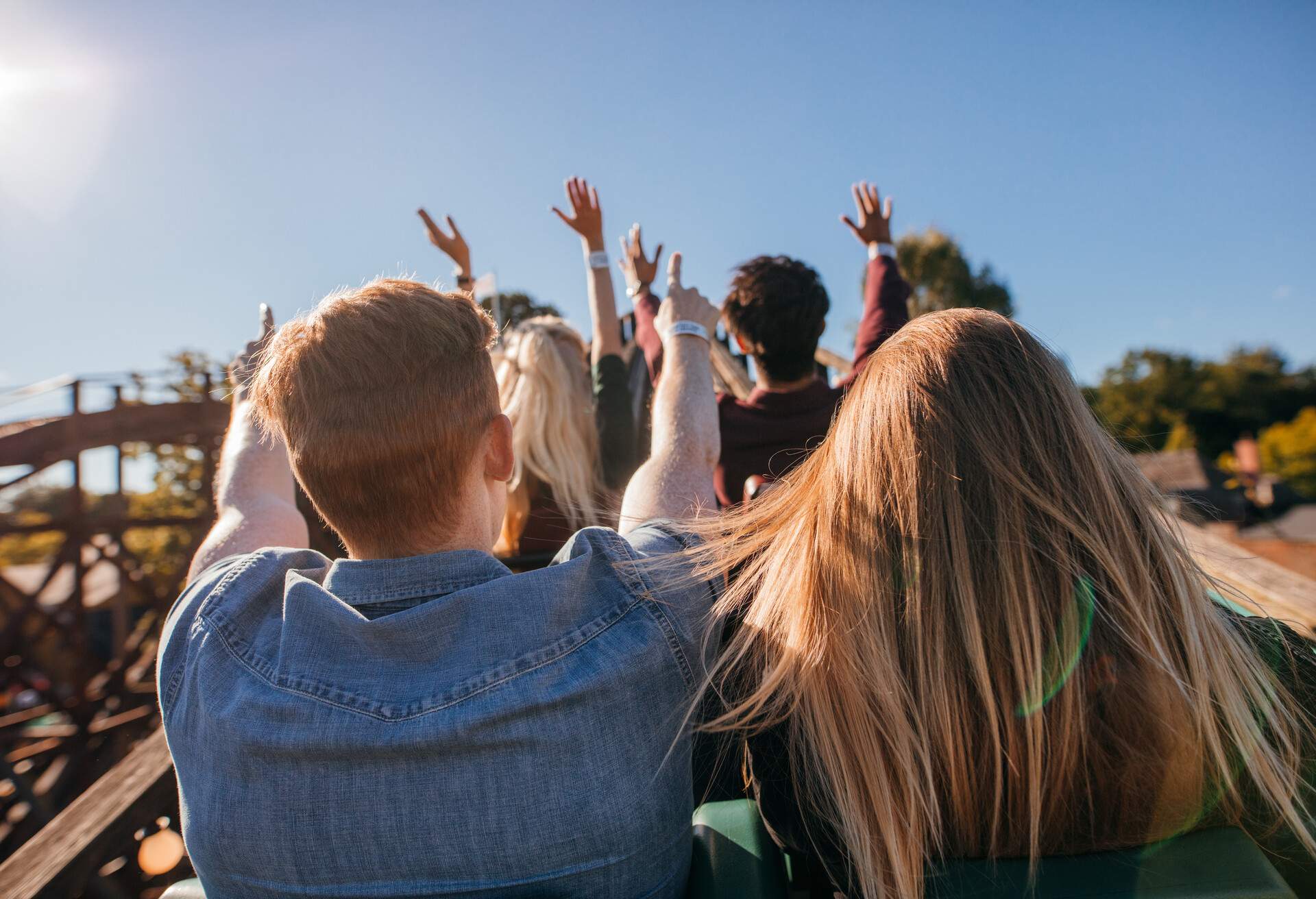 Rear view shot of young people on a thrilling roller coaster ride at amusement park. Group of friends having fun at fair and enjoying on a ride.