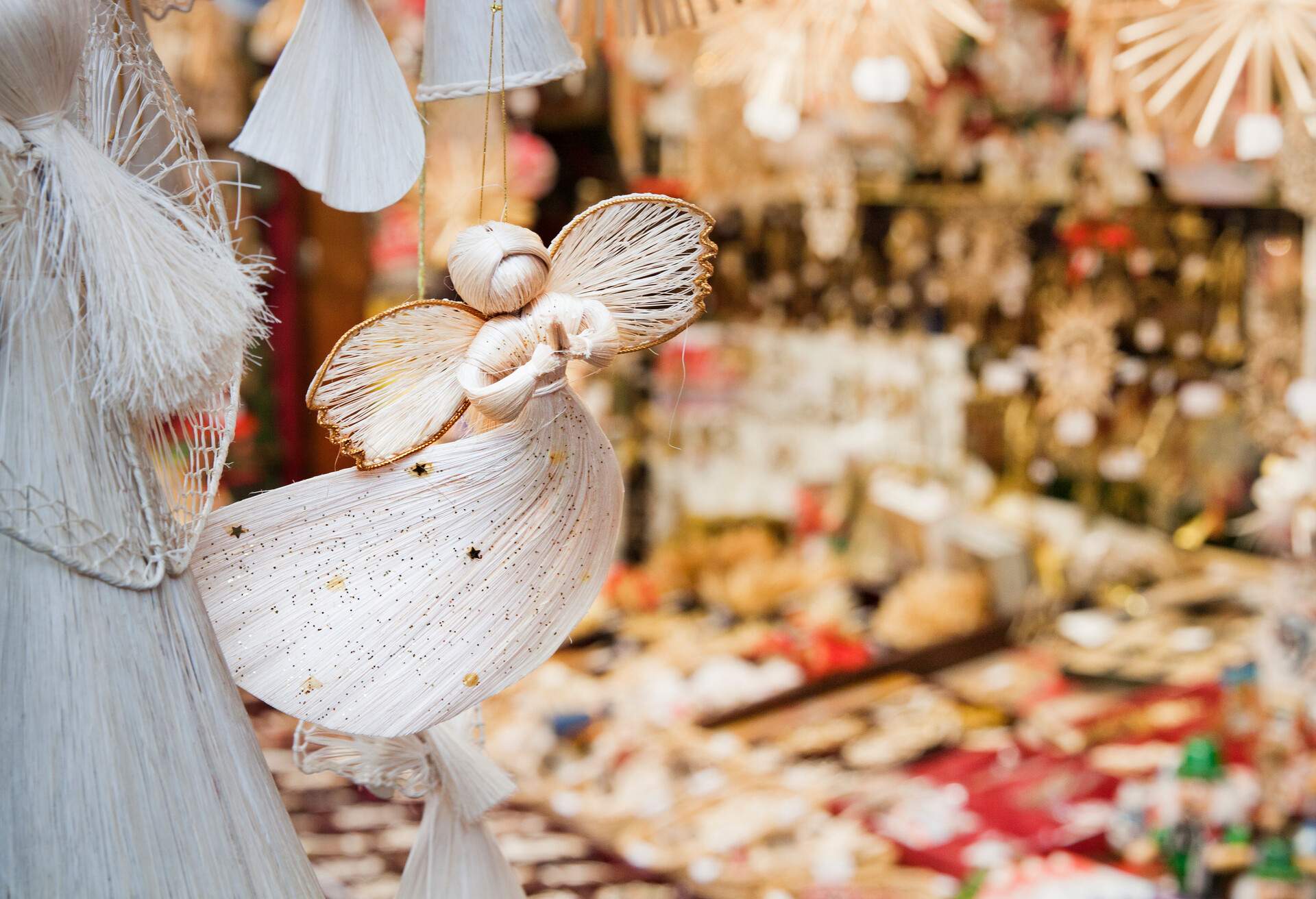 A hanging little angel souvenir decorated with glitter and little stars in the blurry background.