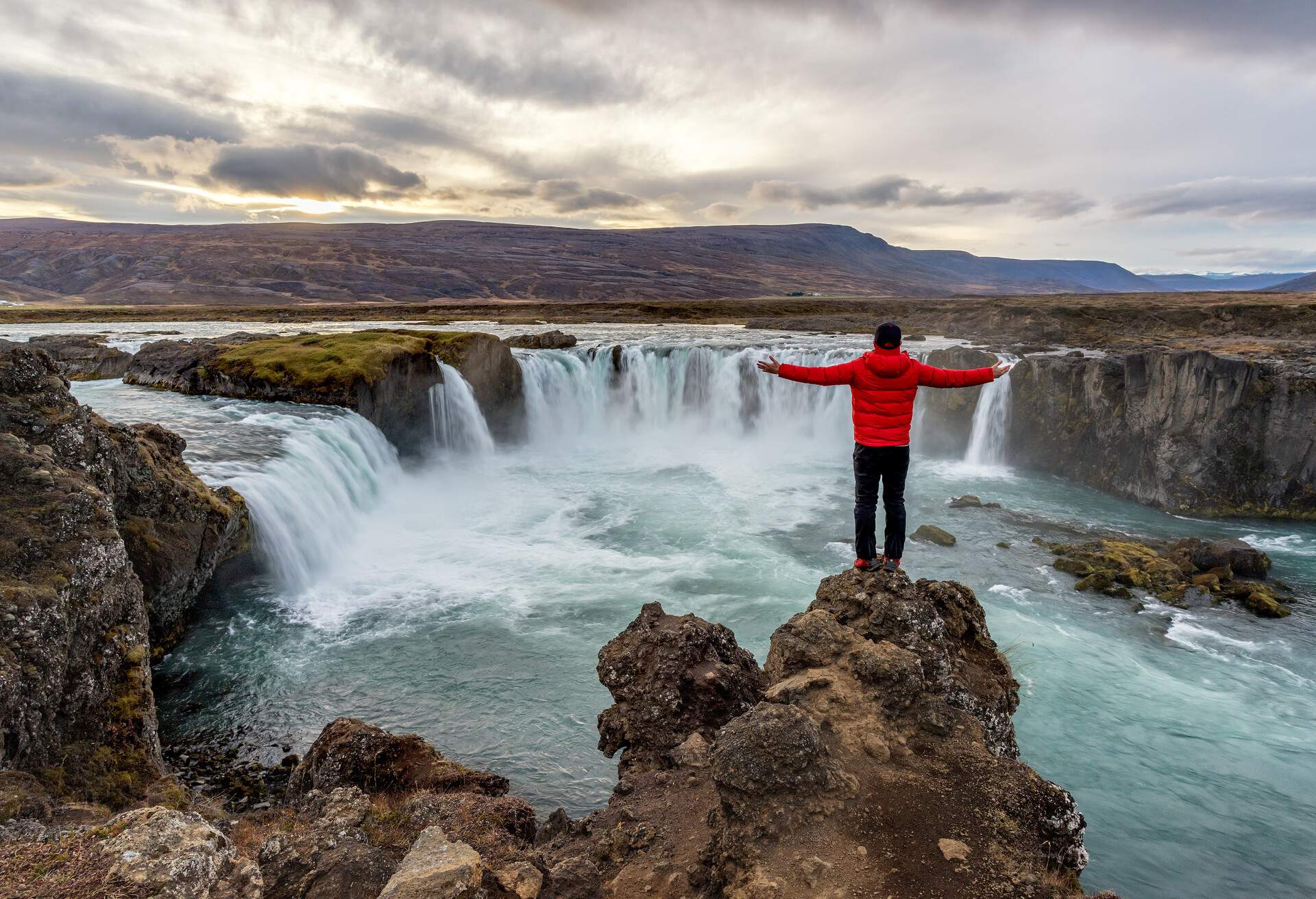 A man standing below Godafoss waterfall, ICELAND