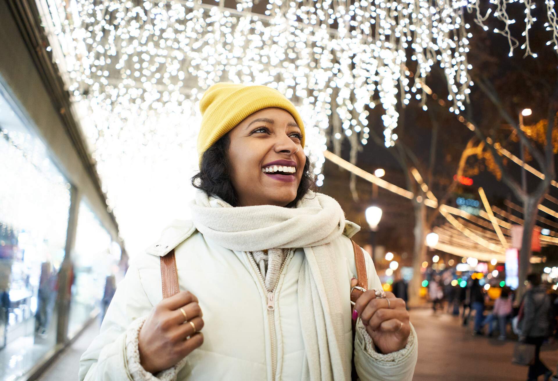 Cheerful African American young woman with big toothy smile standing by Christmas lights amazed by the view outdoors.