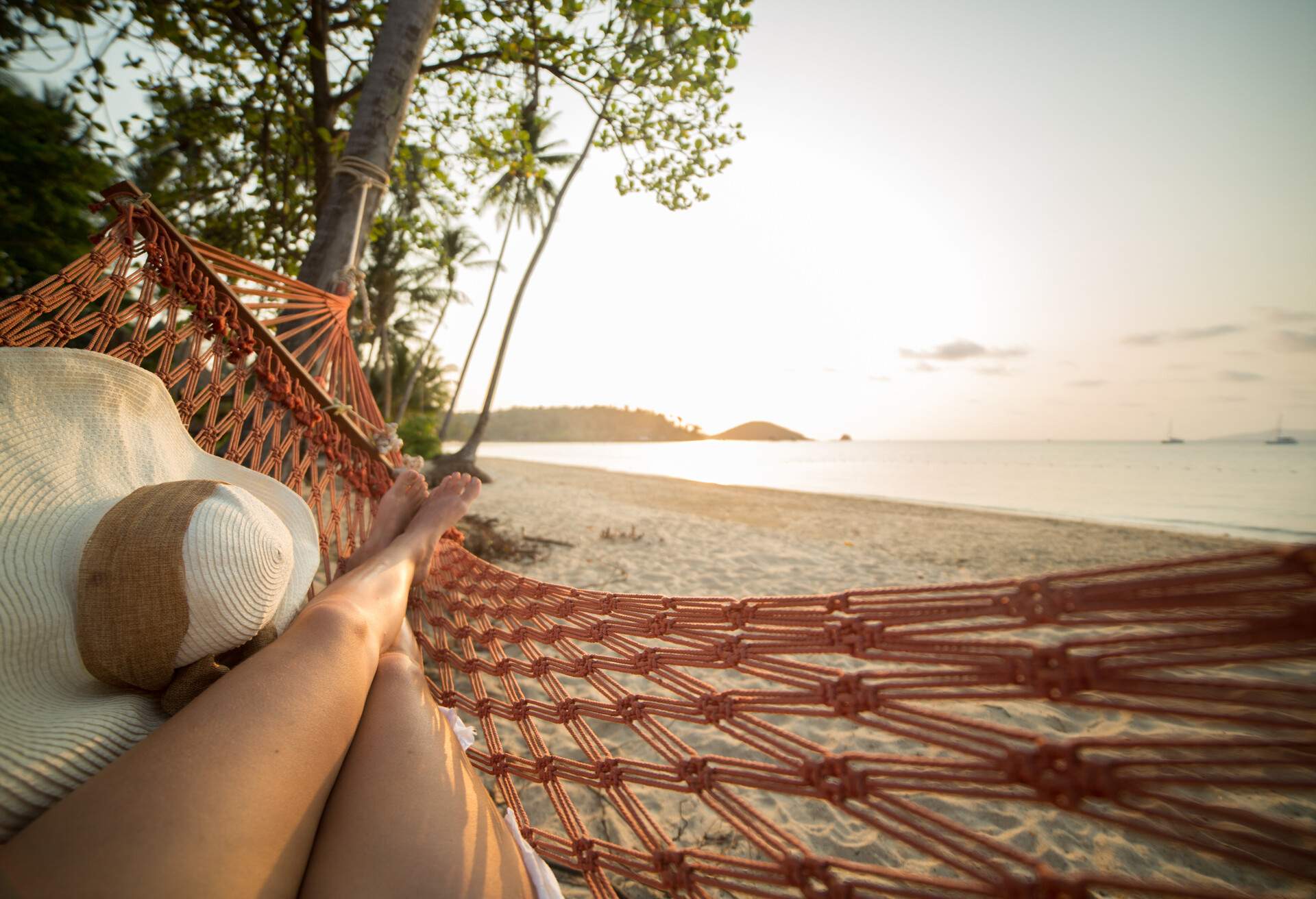 Young woman on a tropical beach in Thailand lying down on a hammock relaxing. Sunset time on the Island. Shot with 5D Mark III, point of view from the woman's perspective.