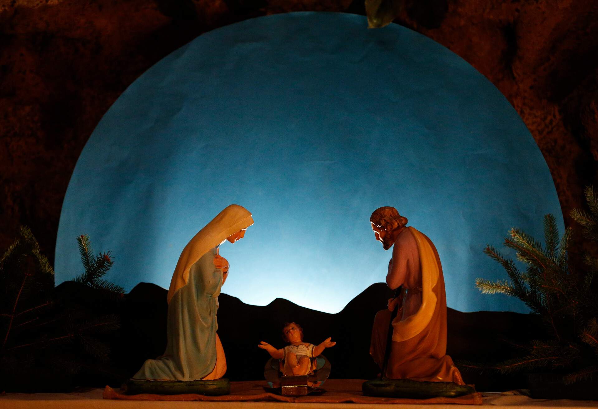Mary and Joseph kneeling beside the infant Jesus with a moon backdrop.
