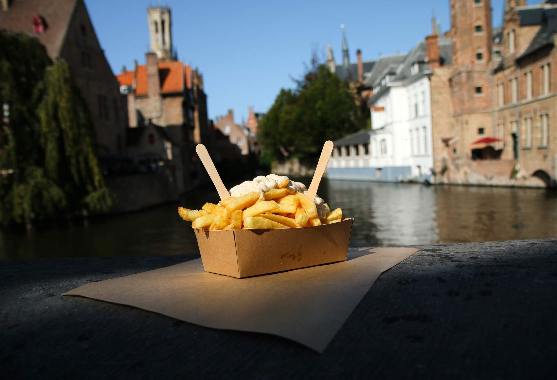 The traditional street food snack, the Belgian Fries with pepper sauce pictured on the wall over the channel in Bruges in Belgium.