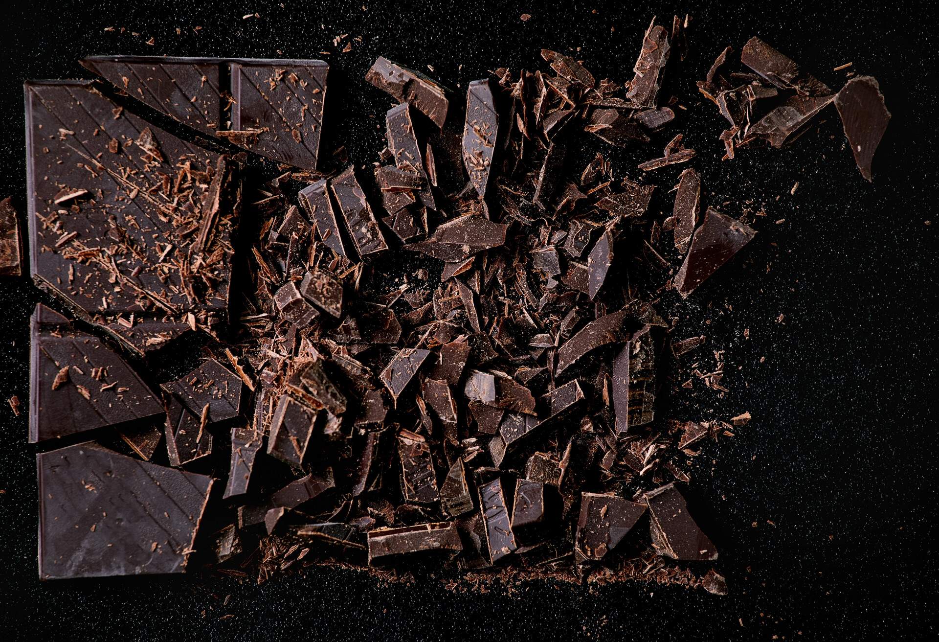 Chopped dark chocolate over black background. Top view of food. Food background.