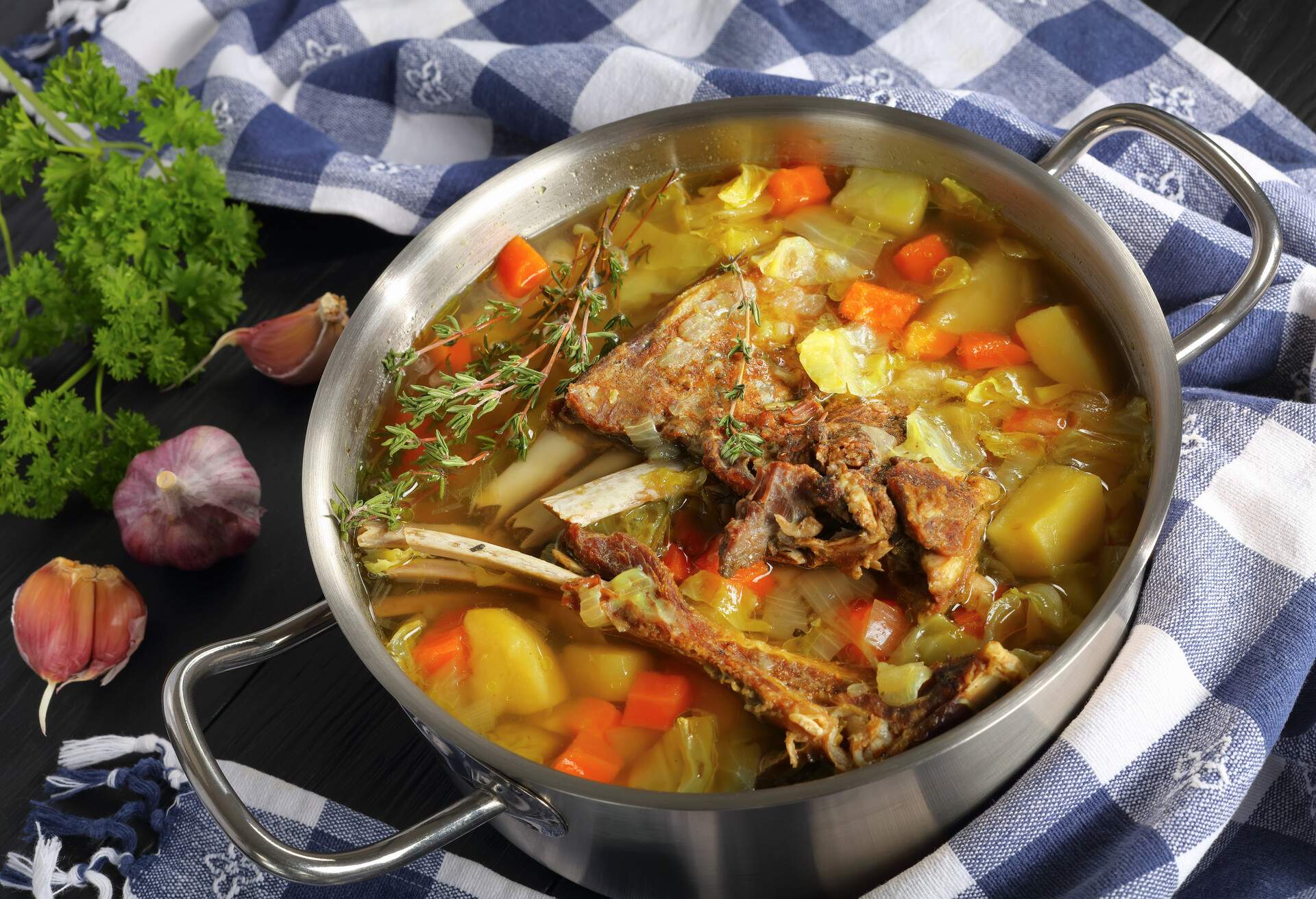 delicious Icelandic Lamb winter hot Soup with vegetables and spices or kjotsupa in a stainless steel casserole pan on wooden table with kitchen towel, traditional recipe, view from above, close-up