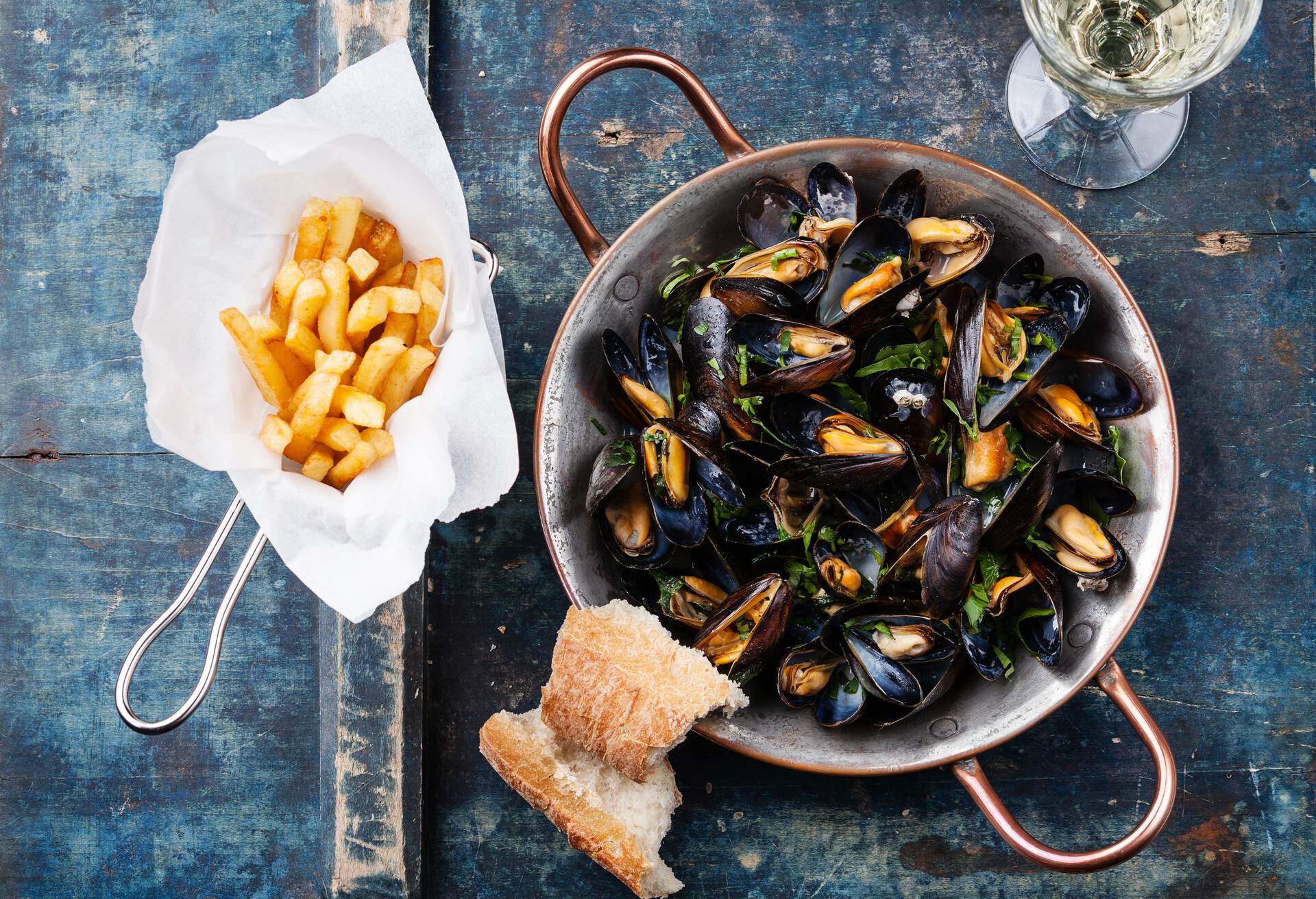 Mussels in copper cooking dish and french fries on blue background