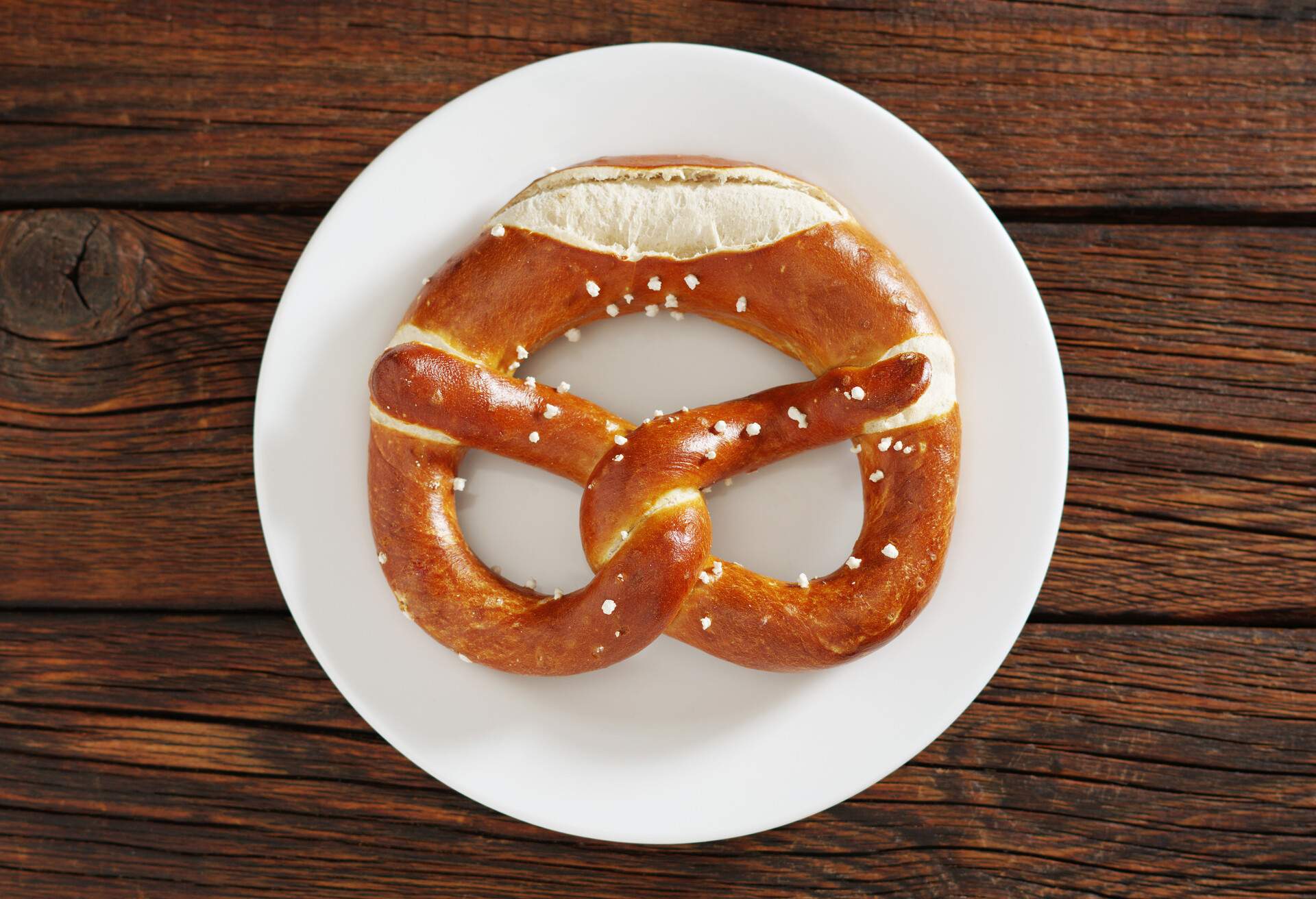 Freshly baked bavarian pretzel on a plate on dark wooden table, top view