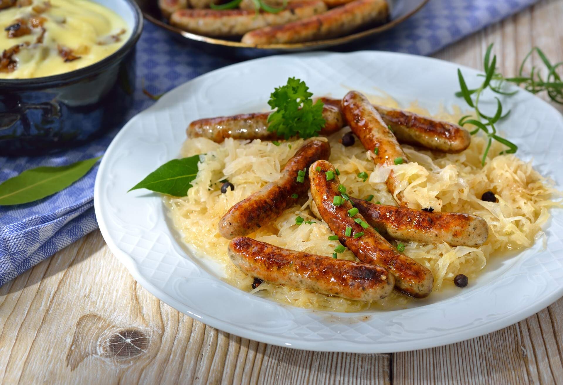 Fried Bavarian sausages from Nuremberg served on sauerkraut, mashed potatoes and some other sausages in the background