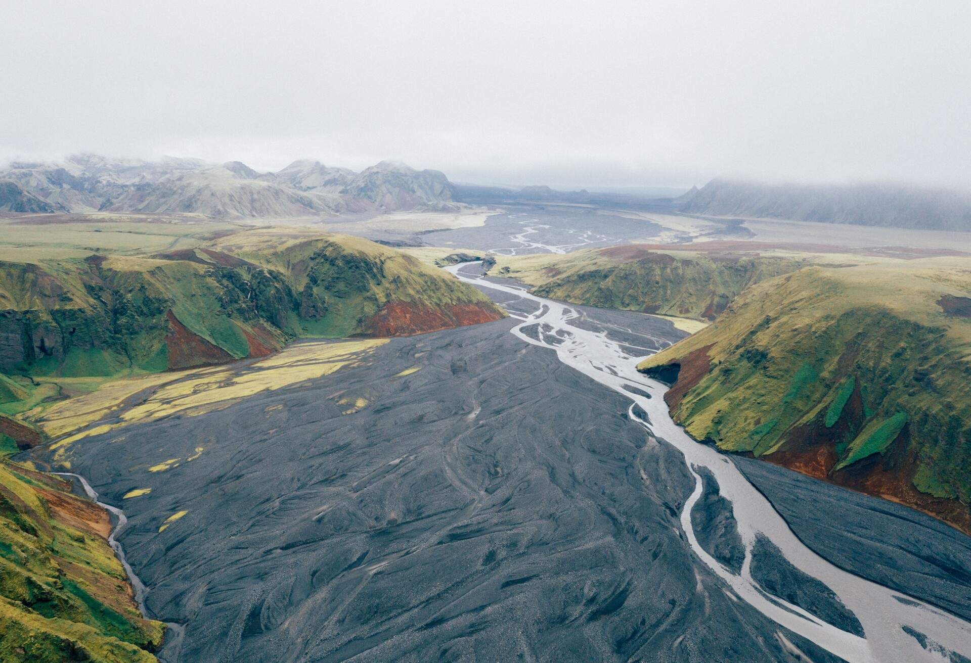An aerial shot of a river flowing trough the green-covered mounts in the Katla Geopark, Iceland