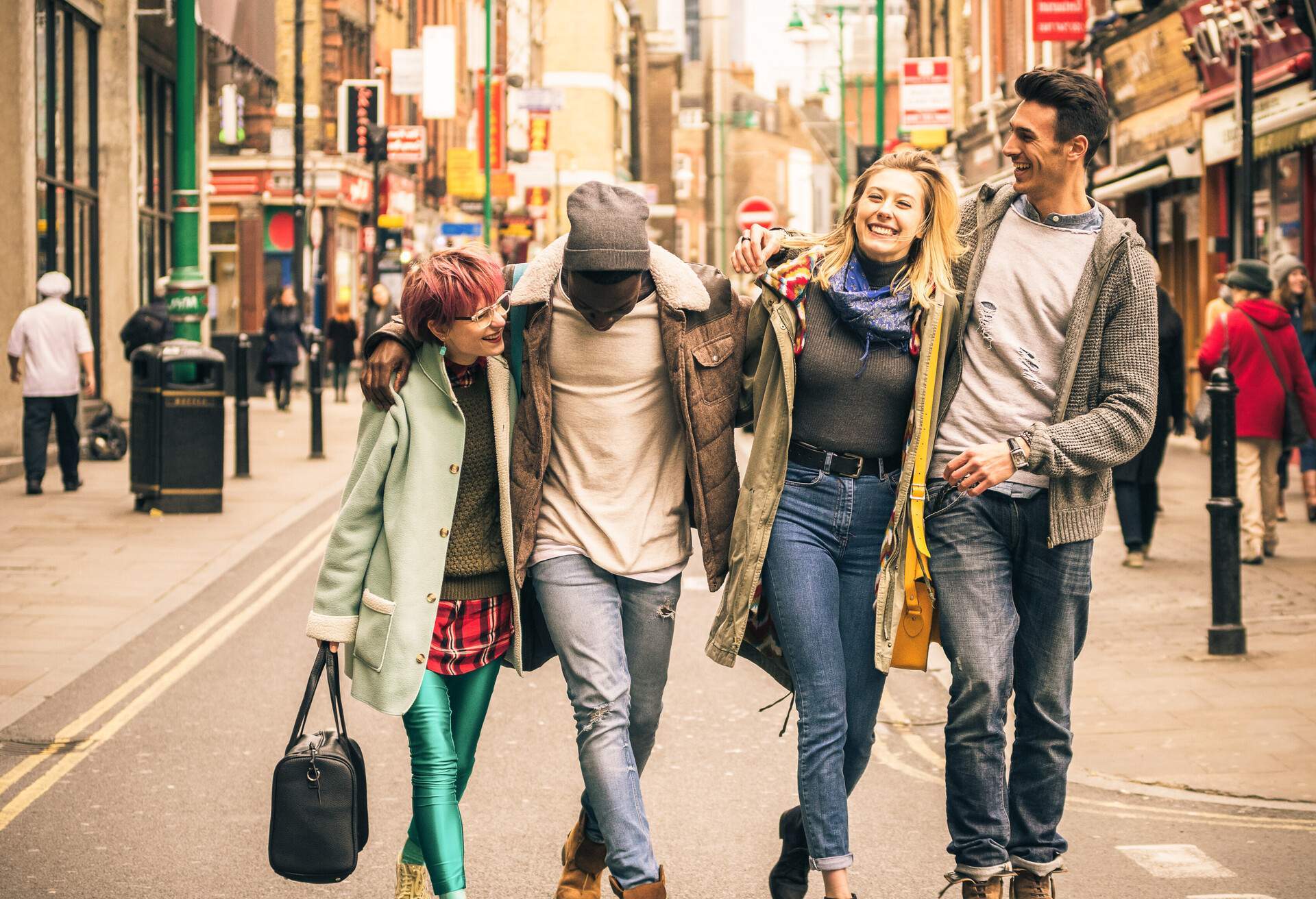 A group of people in winter clothes, hugging in the middle of the street lined with commercial stores.