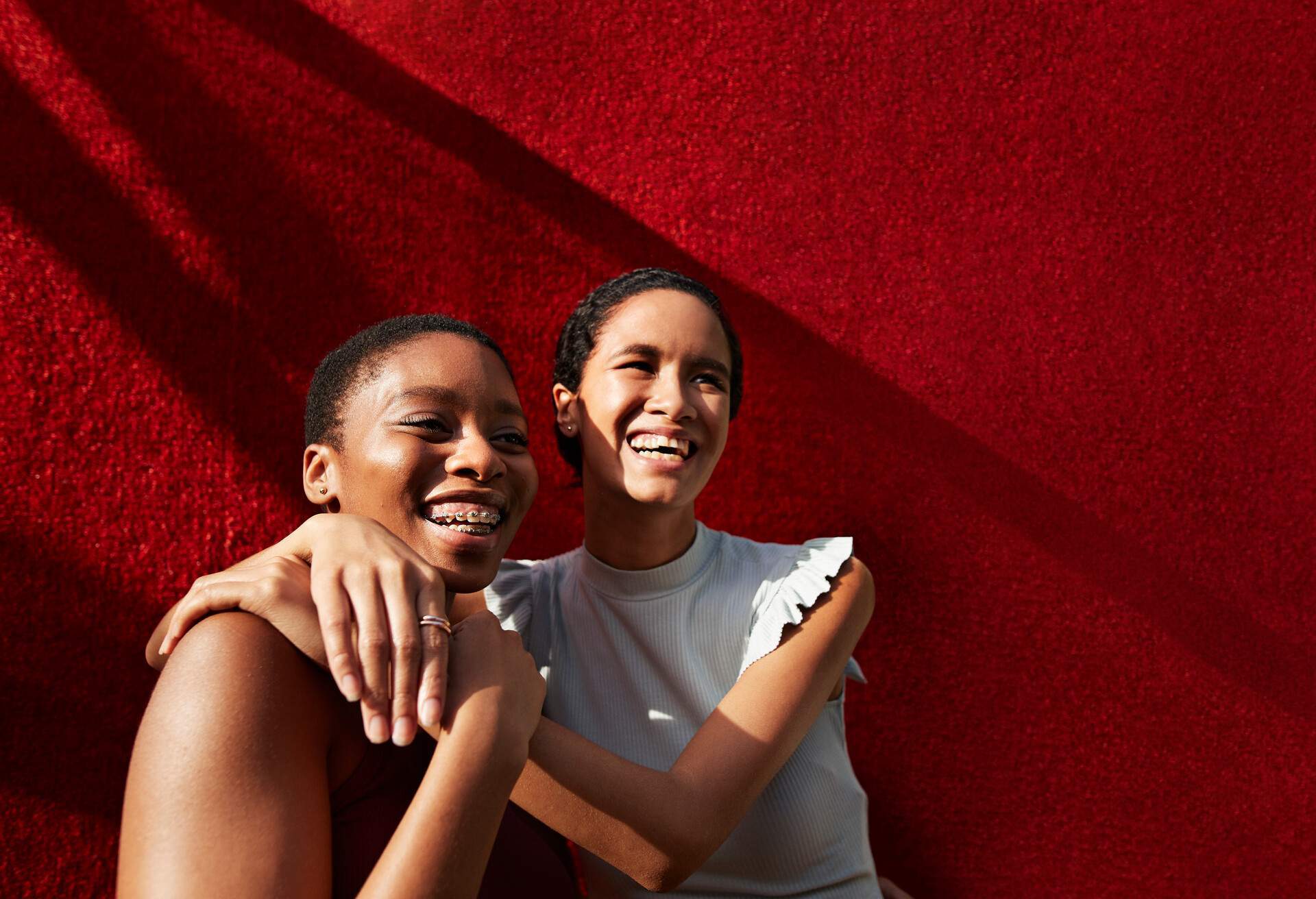 Smiling young woman standing with female friend against red wall 