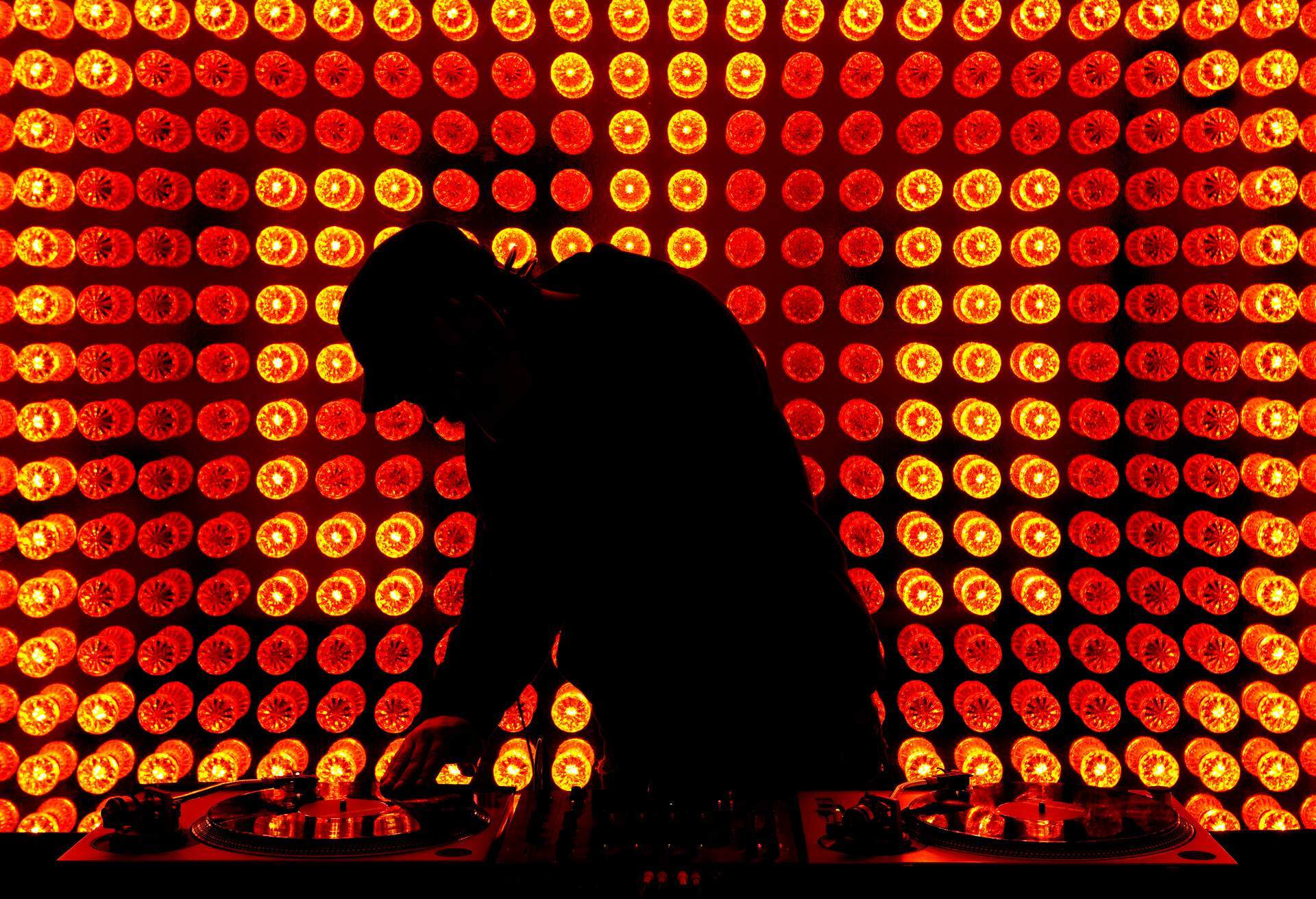 A silhouette of a DJ scratching a vinyl record with a colourful background of round lights.