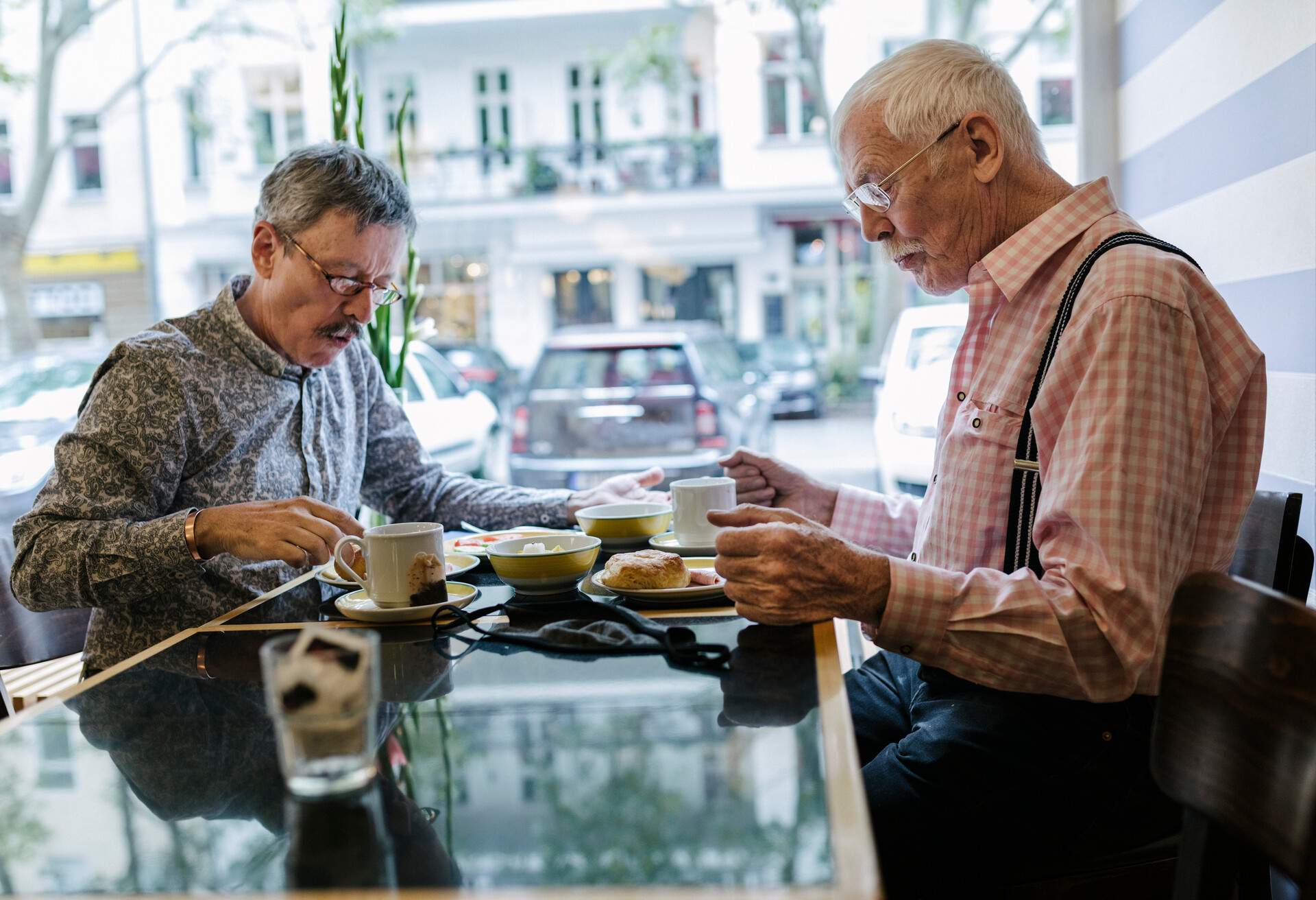 A mature gay couple sitting down for a buffet breakfast together at a hotel they are staying at. 