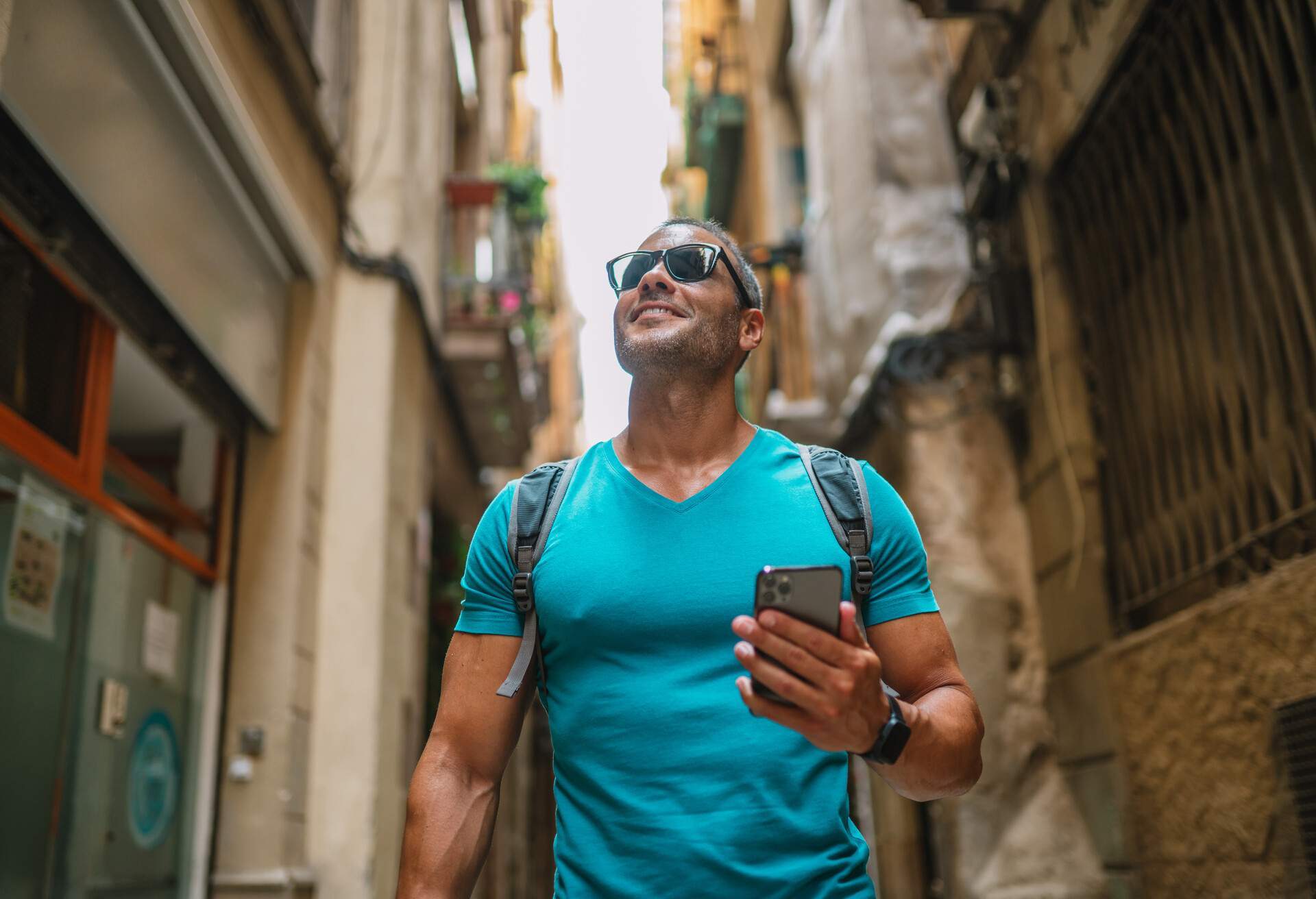 Happy male tourist phone user walking in old town alley an using smartphone. GPS maps, concept. Barcelona, Spain. 
