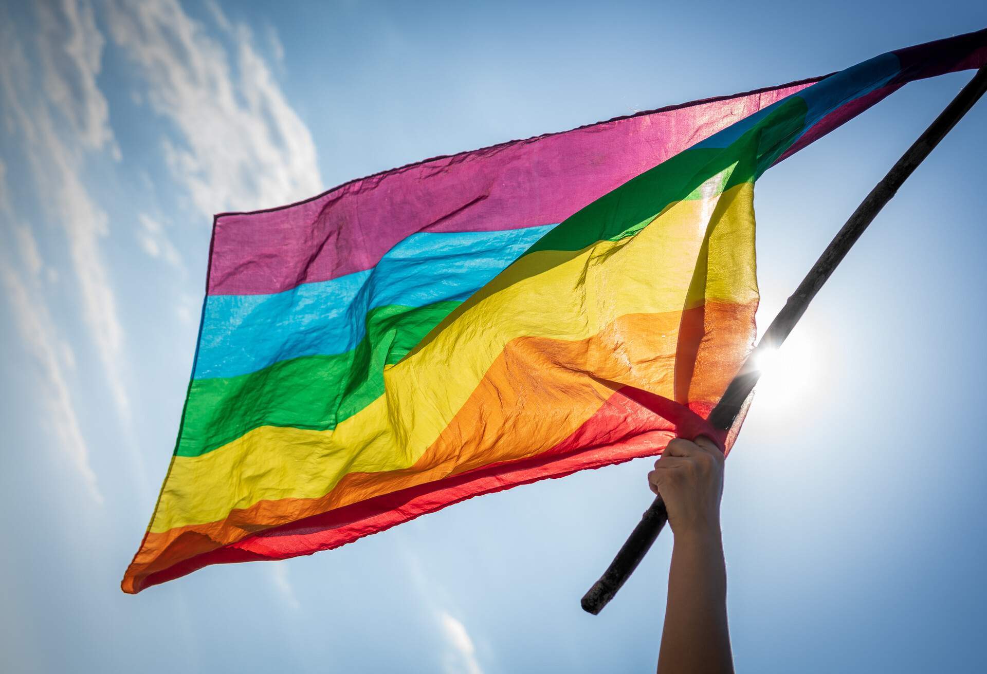 Picture of woman hand waving lgbti flag under the blue sky 
